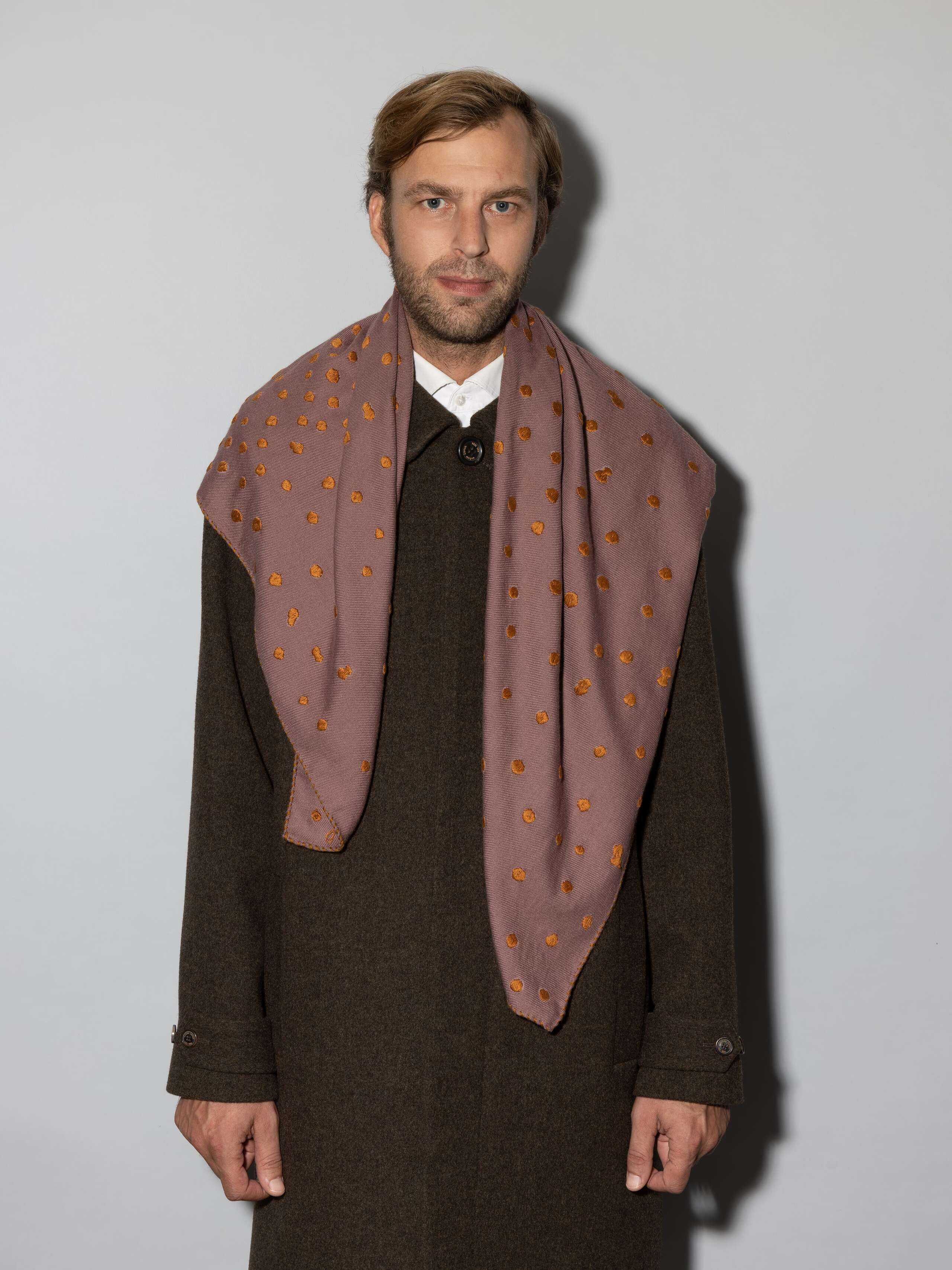 Man wearing Leo wool scarf in a warm cherry wood purple with dot embroidery in warm bronze shades