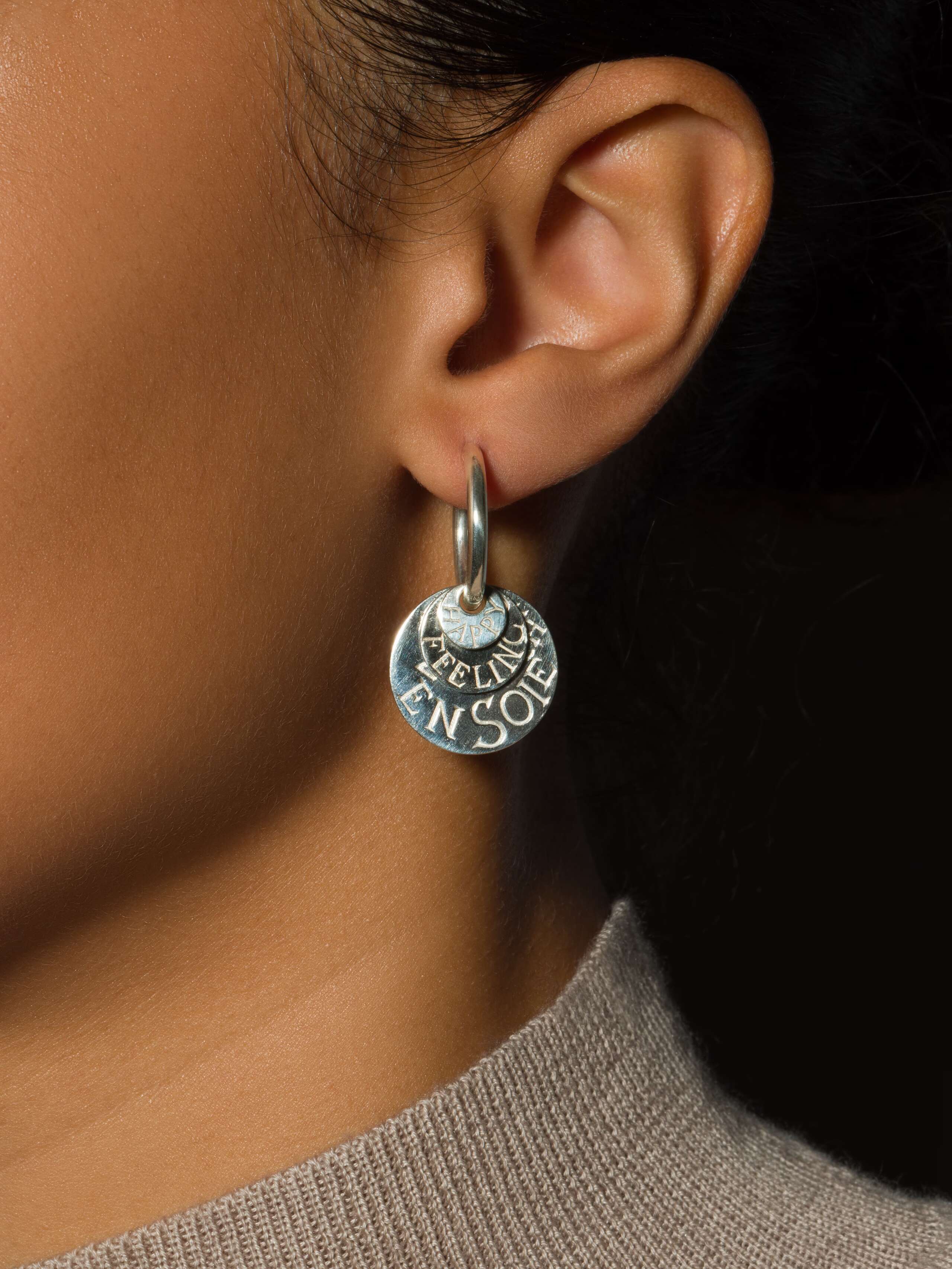 model wears silver earring in creole shape with three round tags 