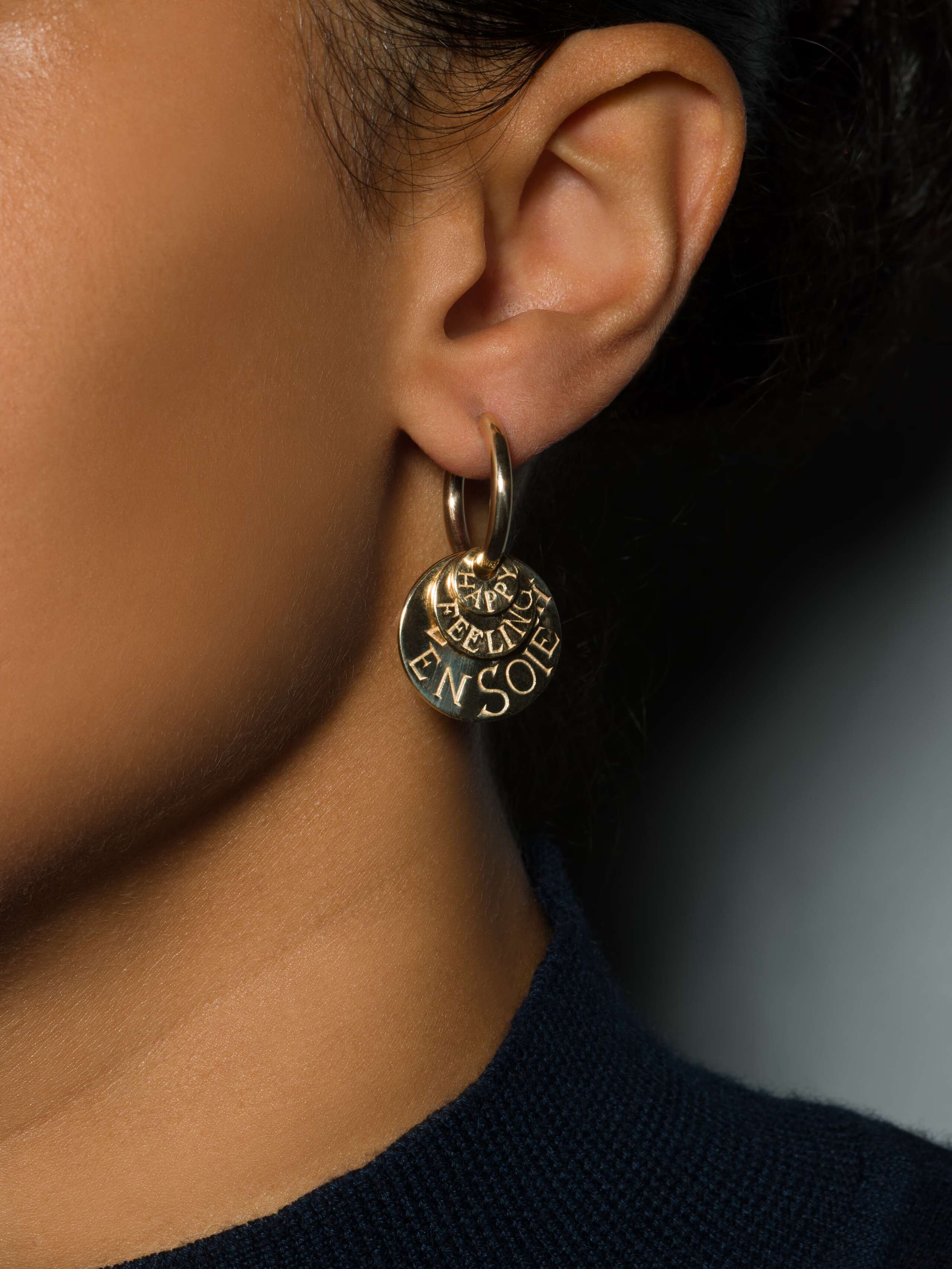 model wears earring in creole shape with three engraved round tags in gold