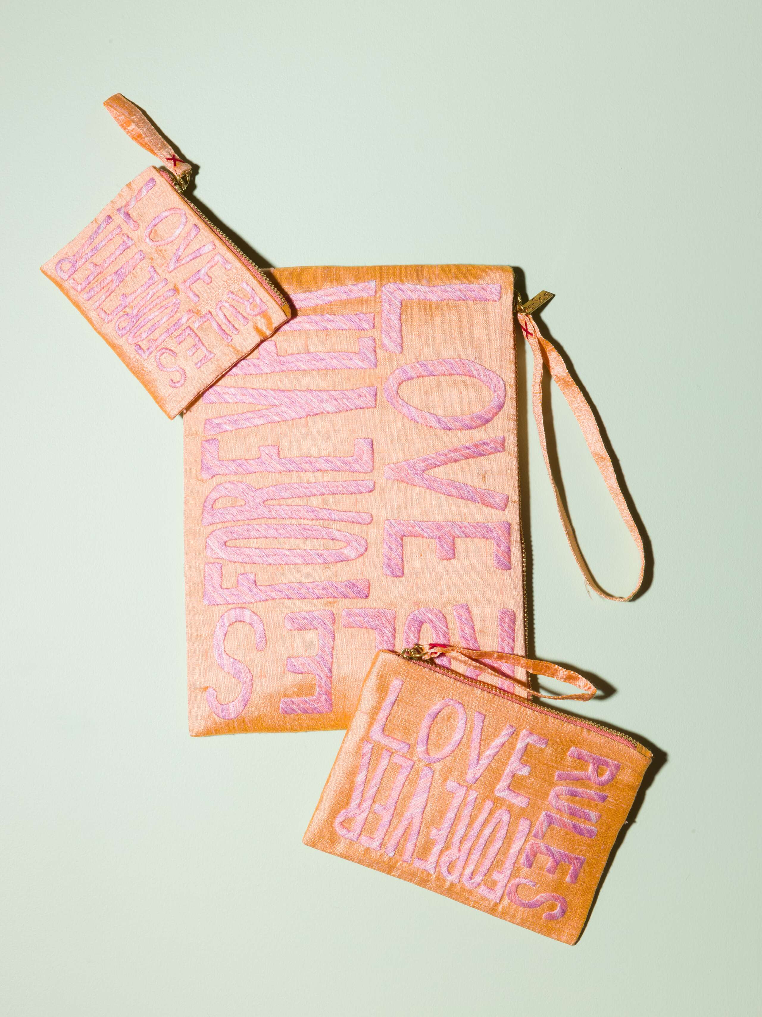 A bundle of beautiful silk clutches in a pale orange with a pearly gloss and beautiful embroidery LOVE RULES FOREVER in pink