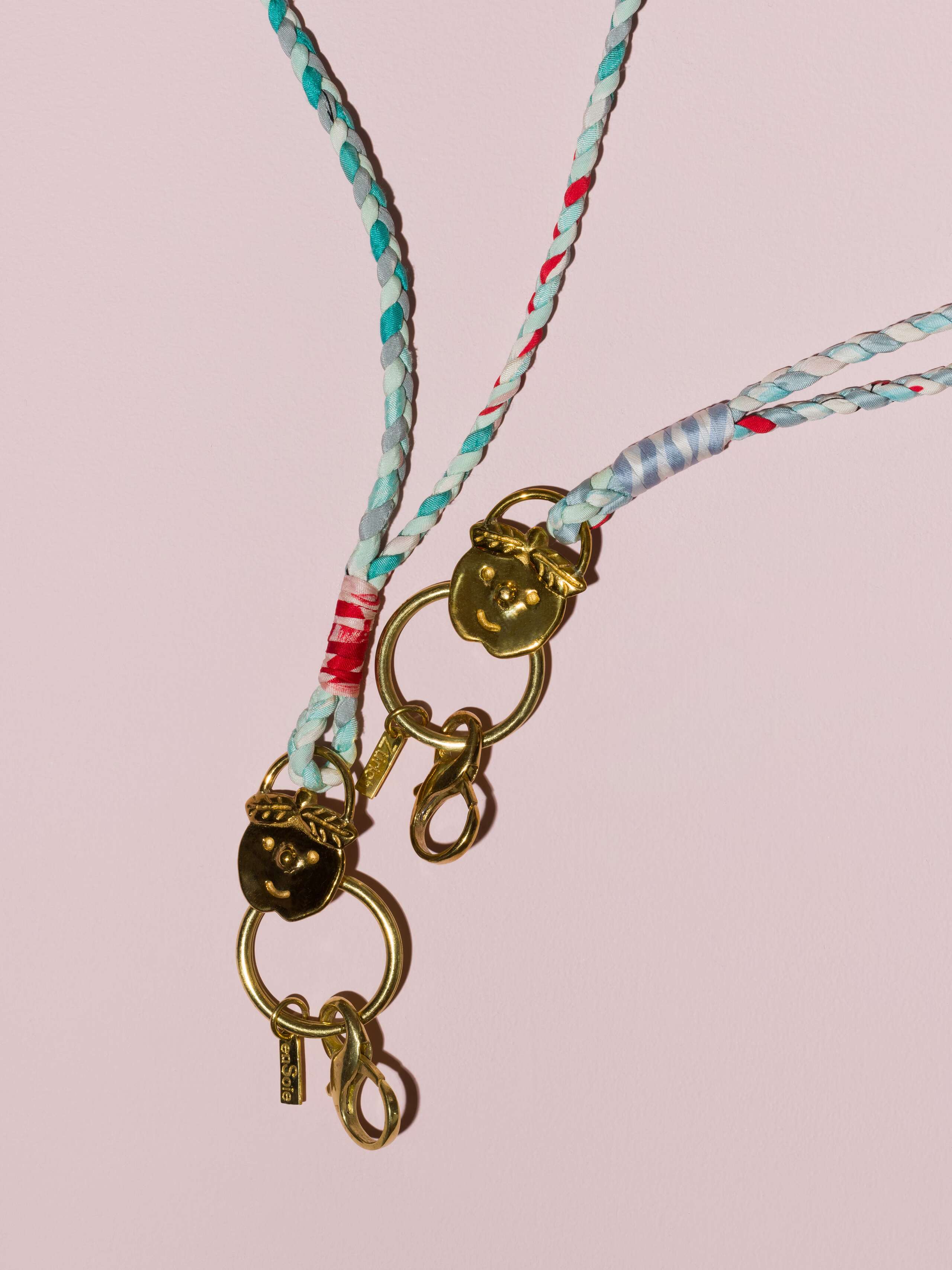 two braided keychains in rose and yellow shades in light blue with a brass tag in shape of a cheeky boys' face