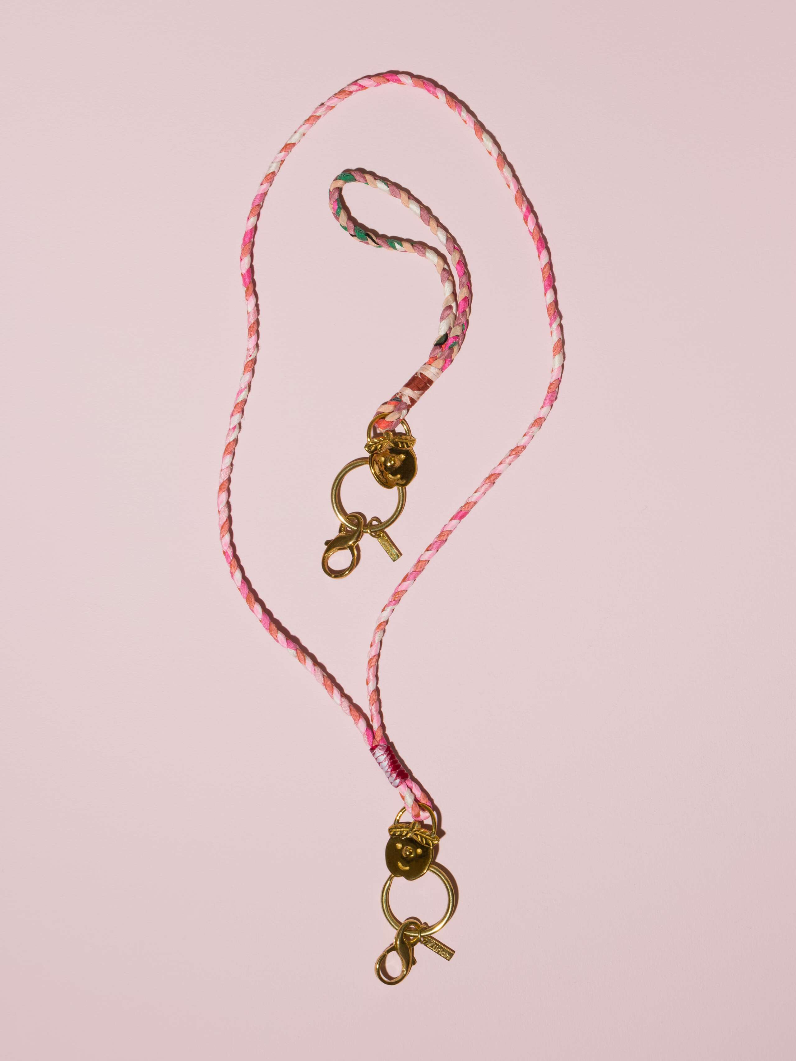 two braided keychains in rose shades in silk with a brass tag in shape of a cheeky boys' face
