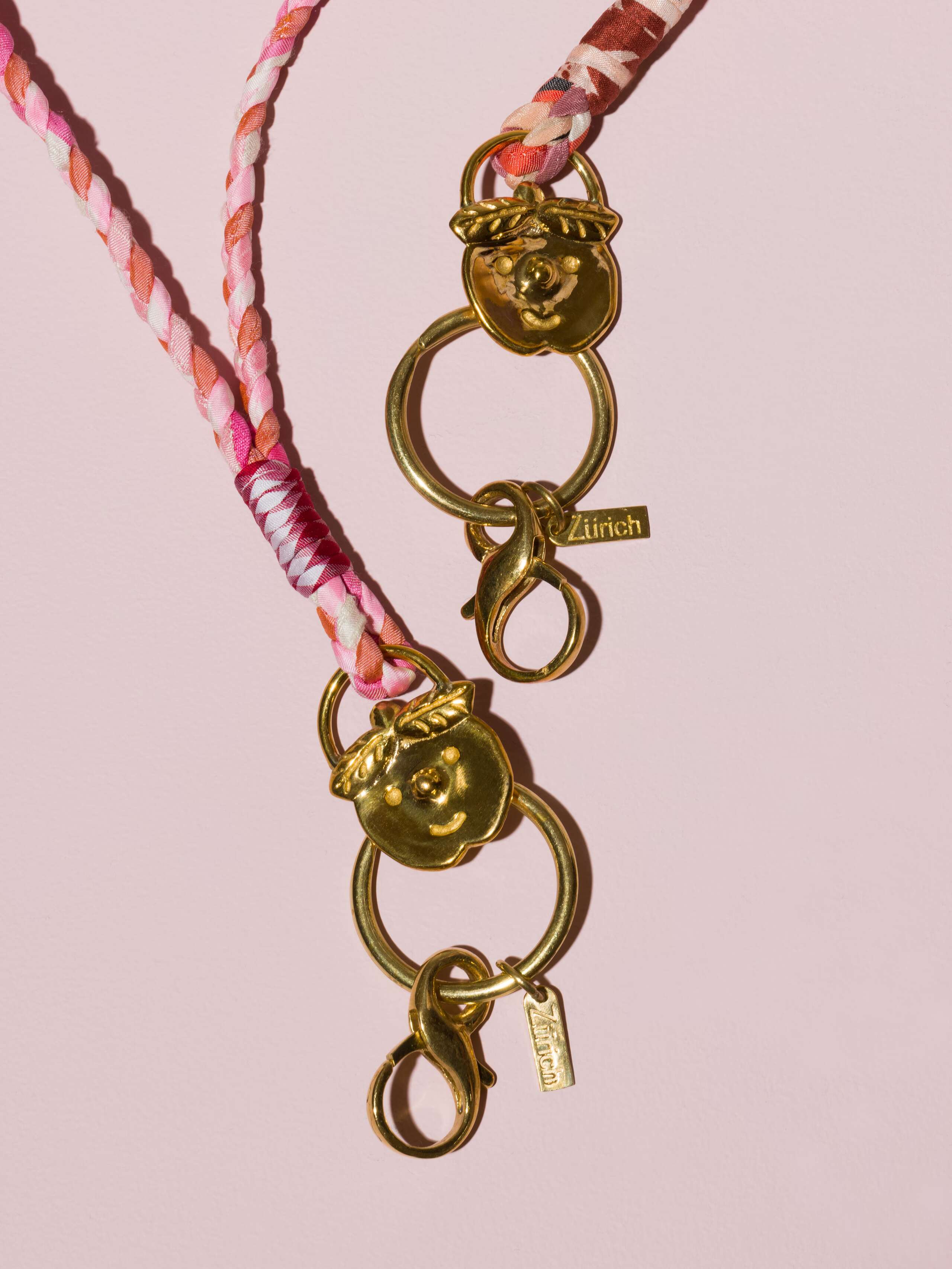 two braided keychains in rose shades in silk with a brass tag in shape of a cheeky boys' face