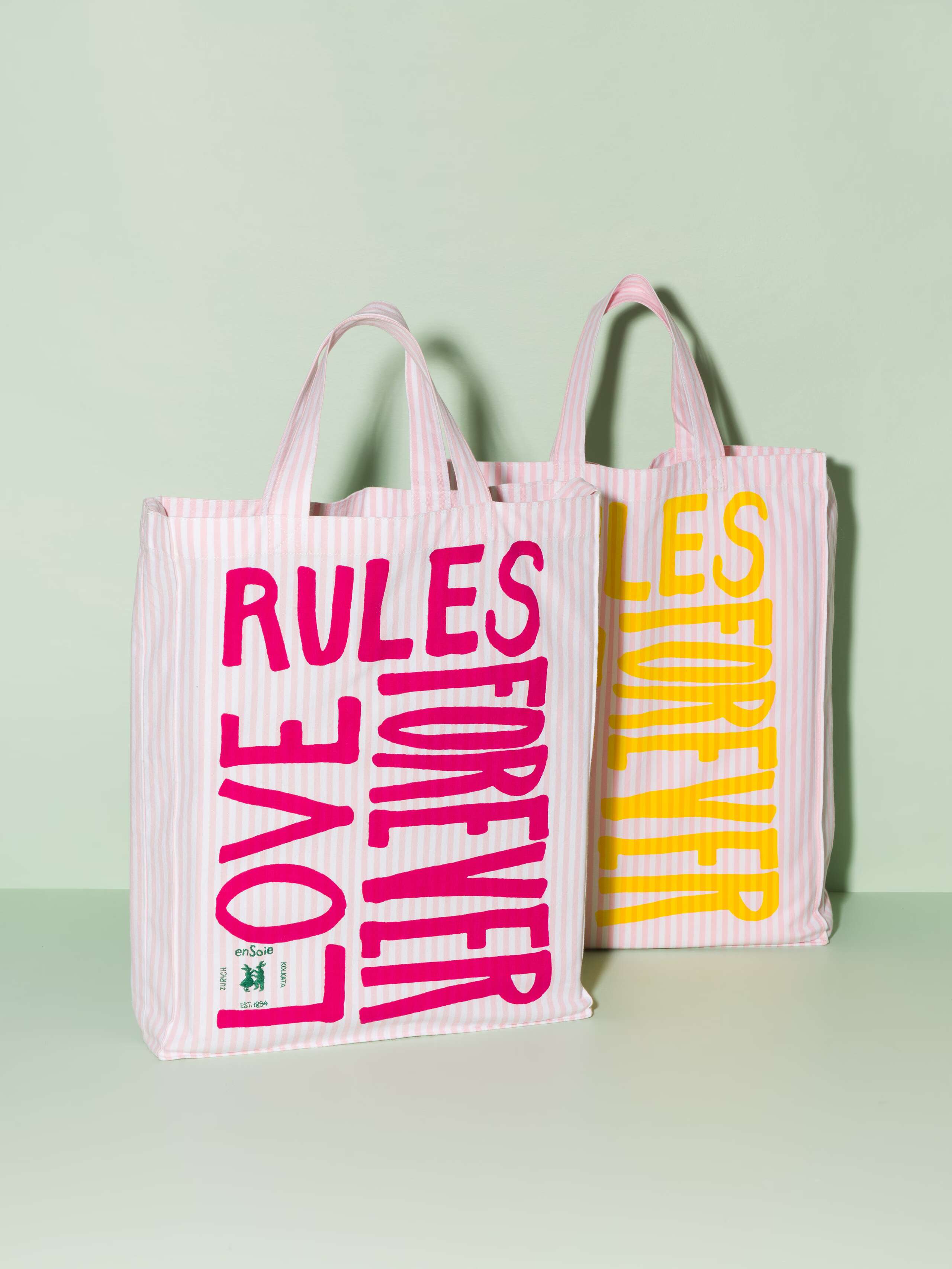 Two cotton tote bags with a pink stripe pattern and a pink and yellow print that says "Love rules forever"