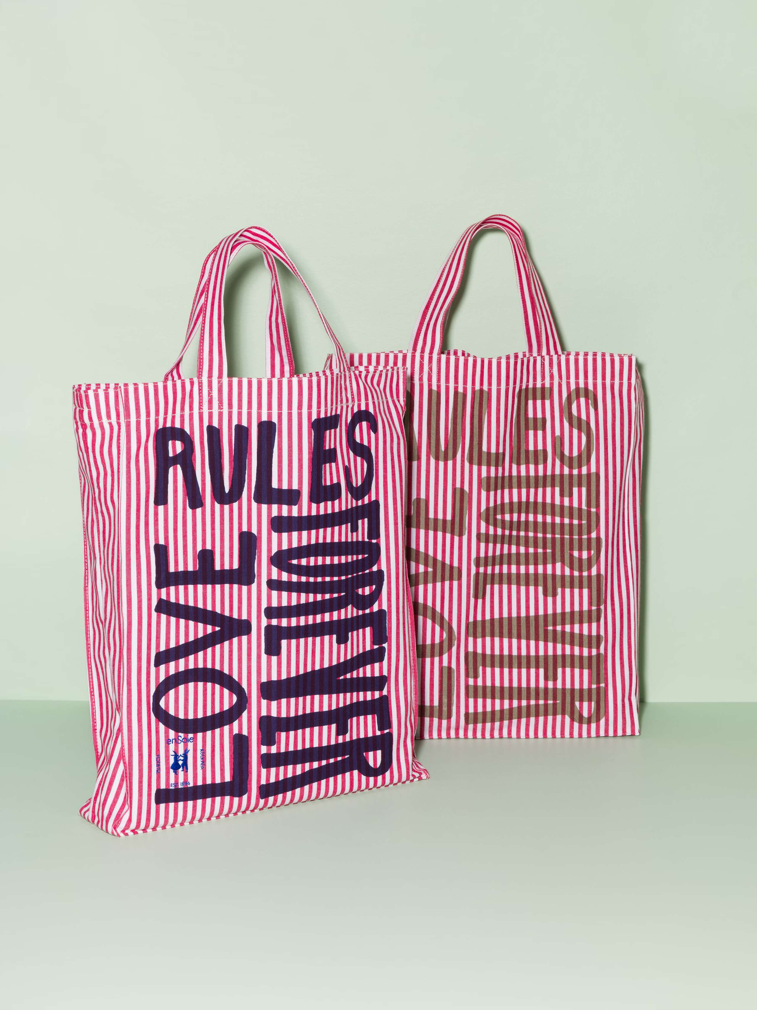 Two cotton tote bags with a red stripe pattern and a beige and navy print that says "Love rules forever"