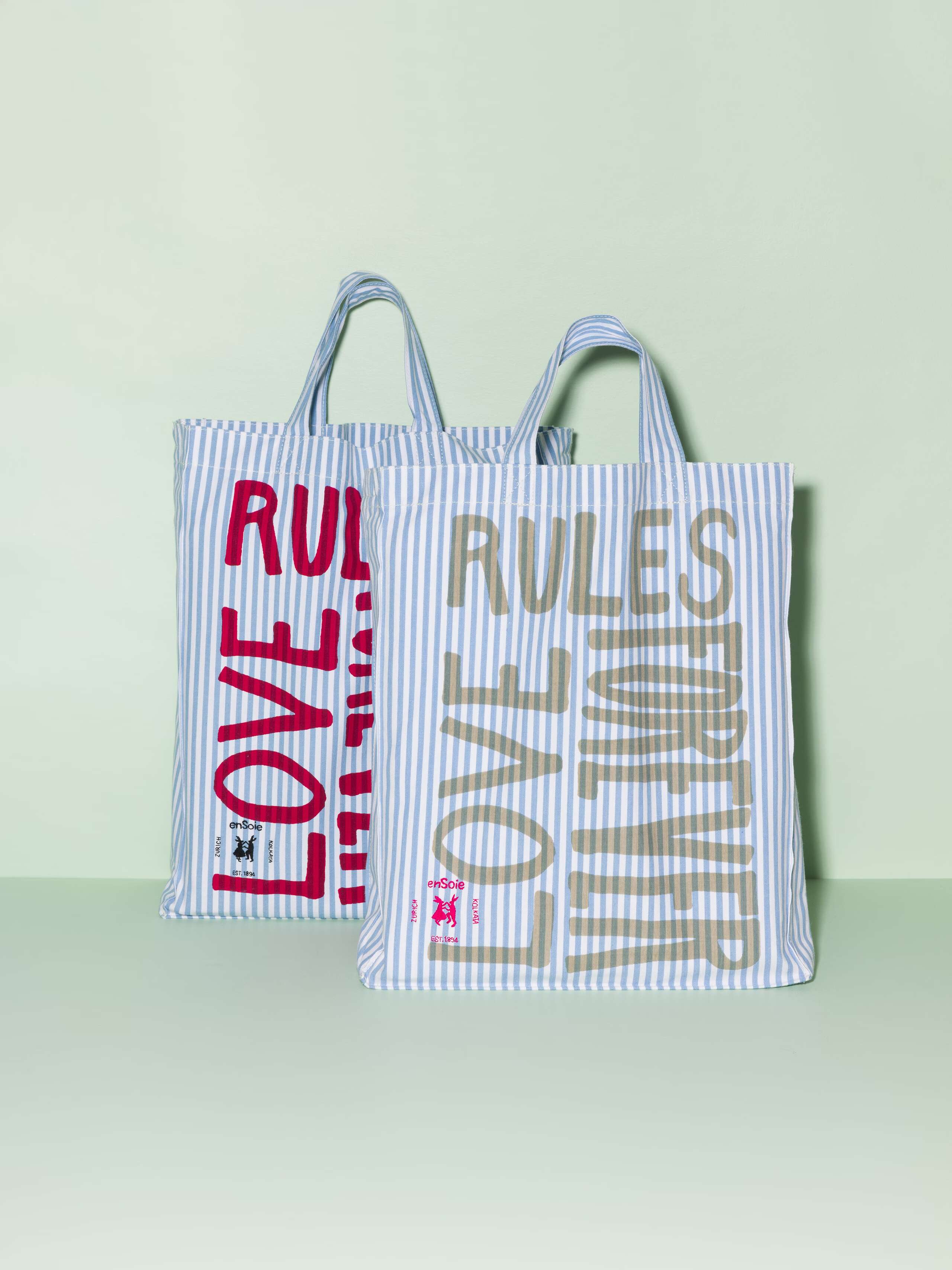 Two cotton tote bags with a light blue stripe pattern and a red and beige print that says "Love rules forever"