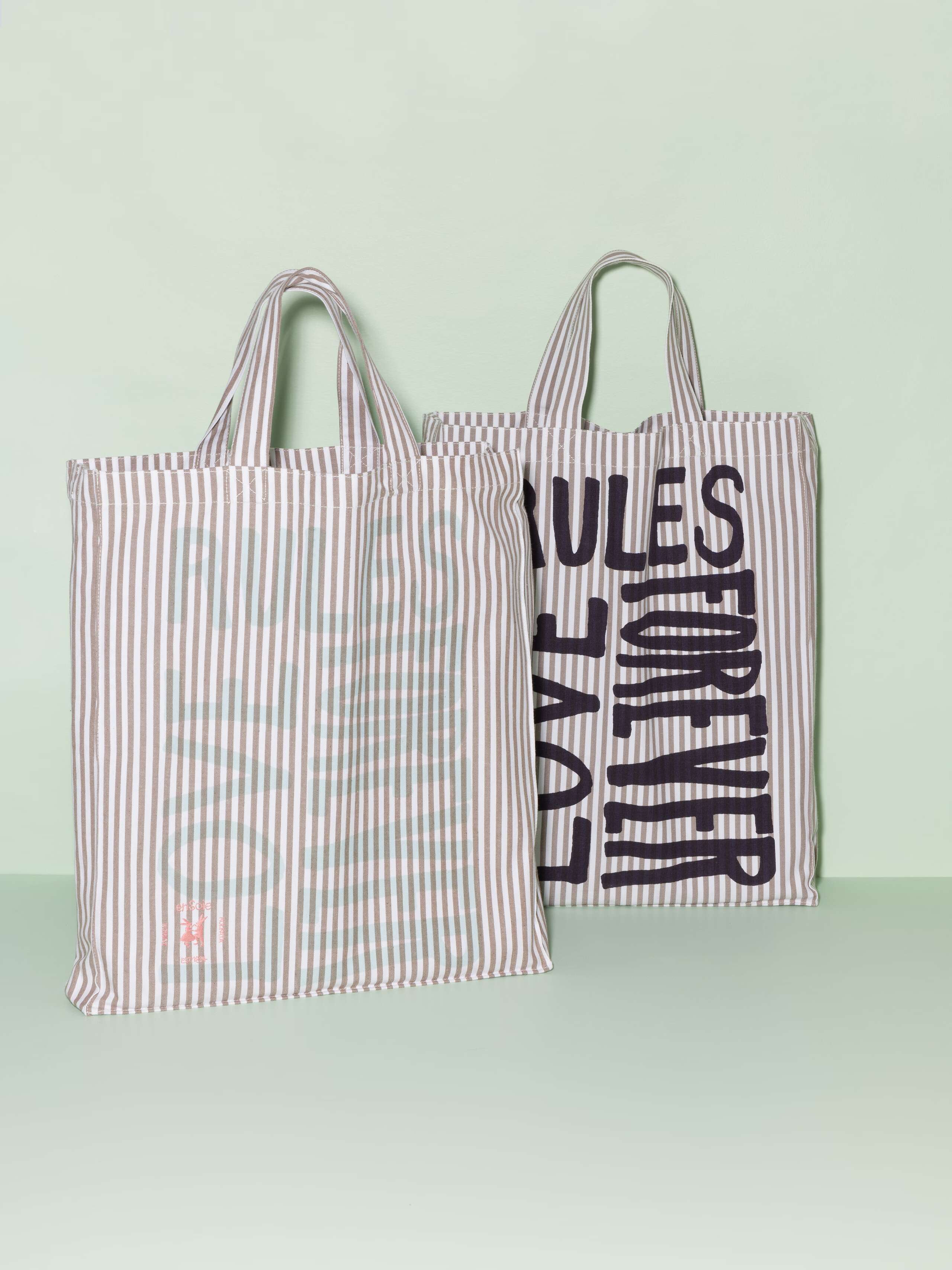 Two cotton tote bags with a beige stripe pattern and a mint and navy print that says "Love rules forever"