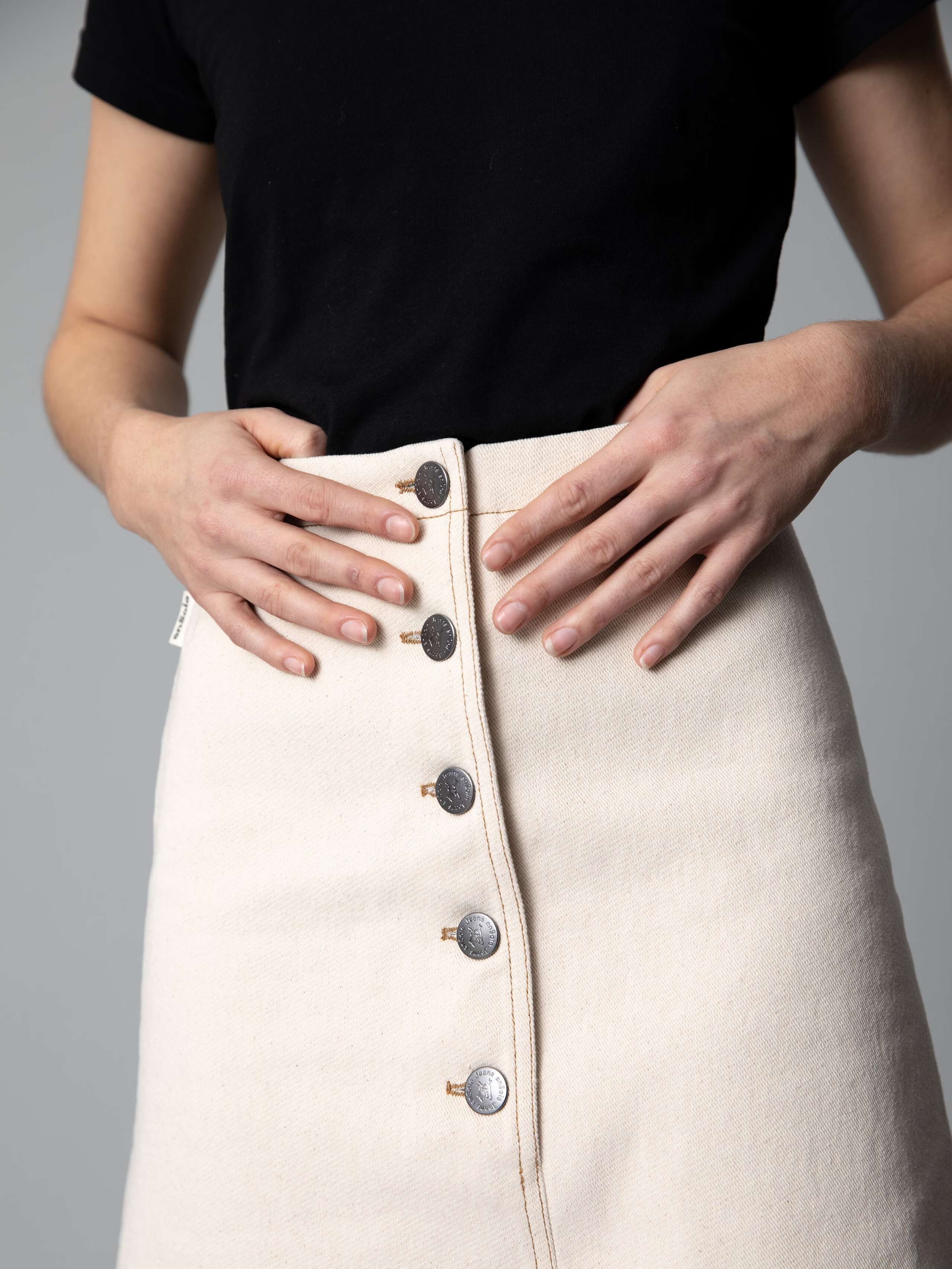 Detail of a beautiful a-line denim skirt in an ecru colour shade combined with black ballerina flats and a black t-shirt