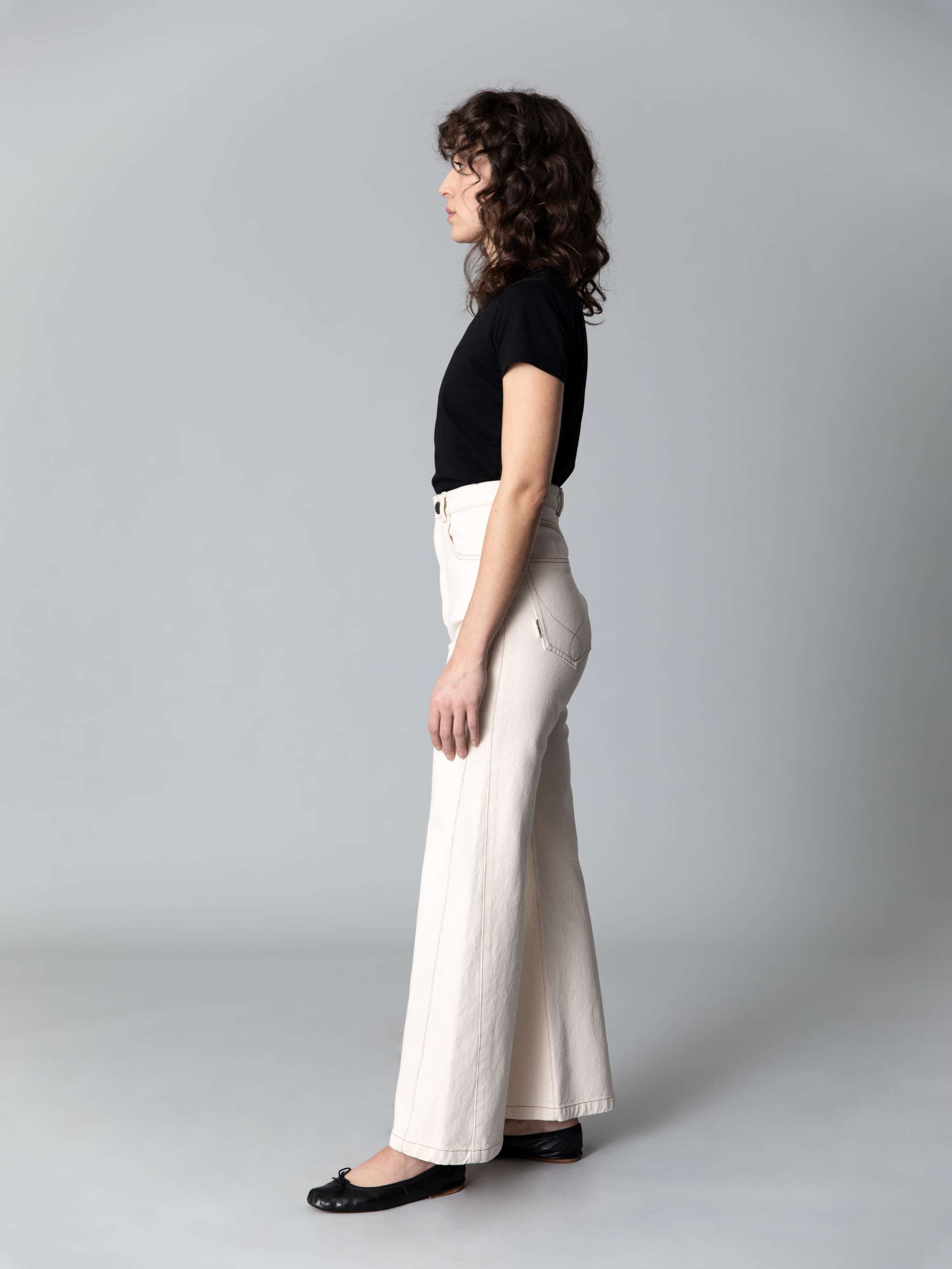 Model with dark hair, blue eyes and light skin is wearing a black cotton shirt and beautiful high waist jeans in a ecru colour
