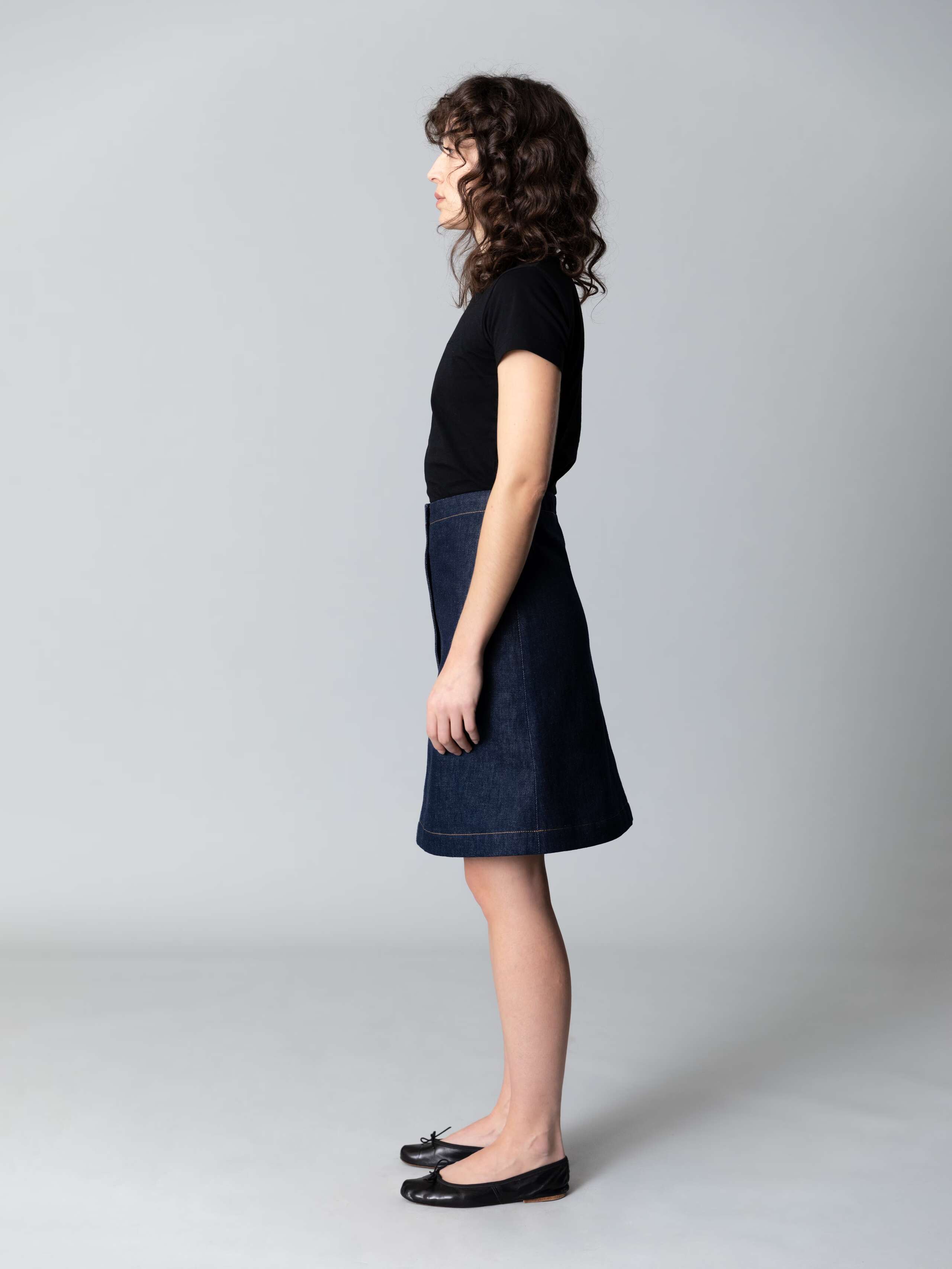 Model is wearing a beautiful a-line denim skirt combined with a black shirt and black ballerina flats