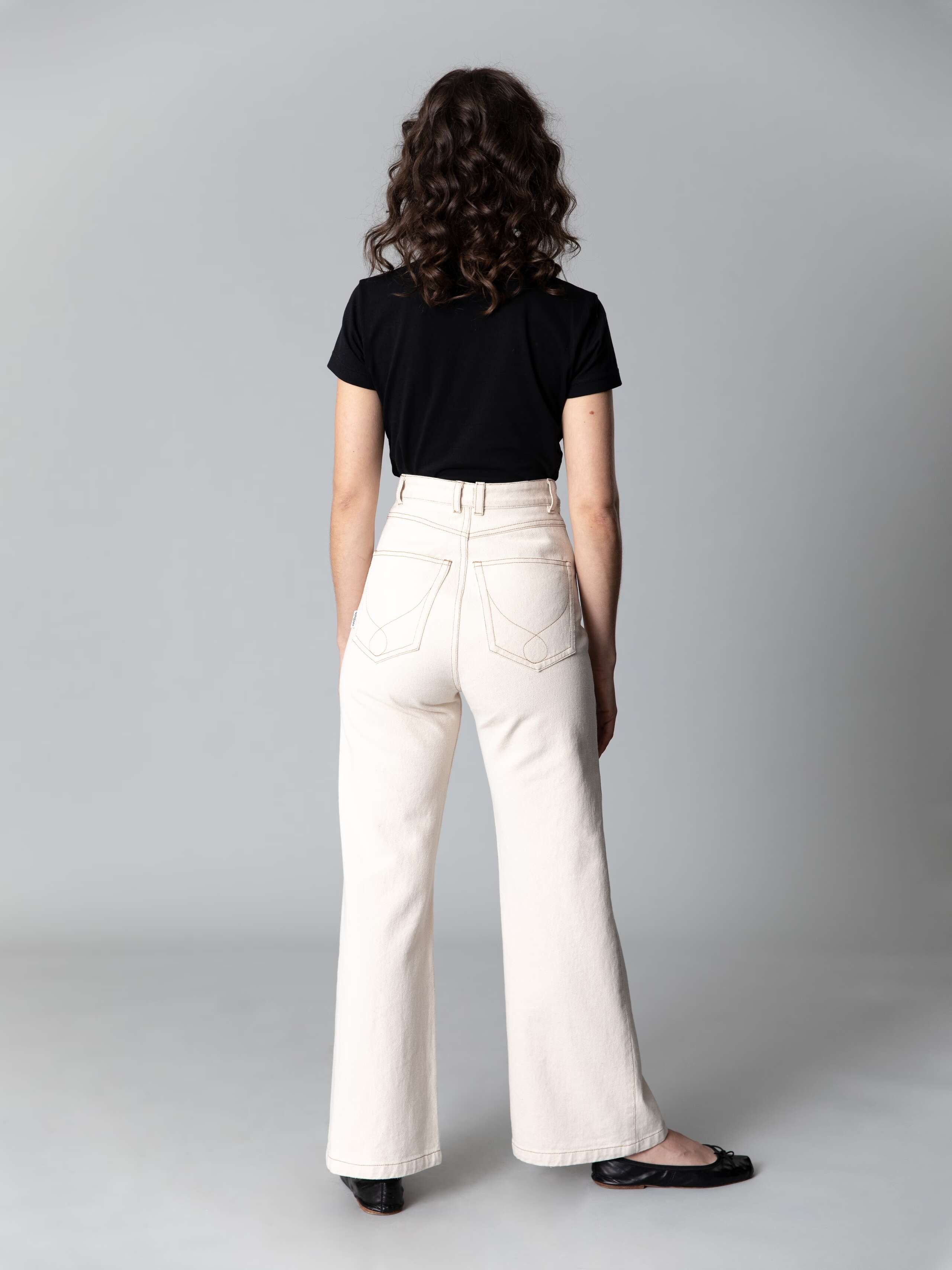 Model with dark hair, blue eyes and light skin is wearing a black cotton shirt and beautiful high waist jeans in a ecru colour