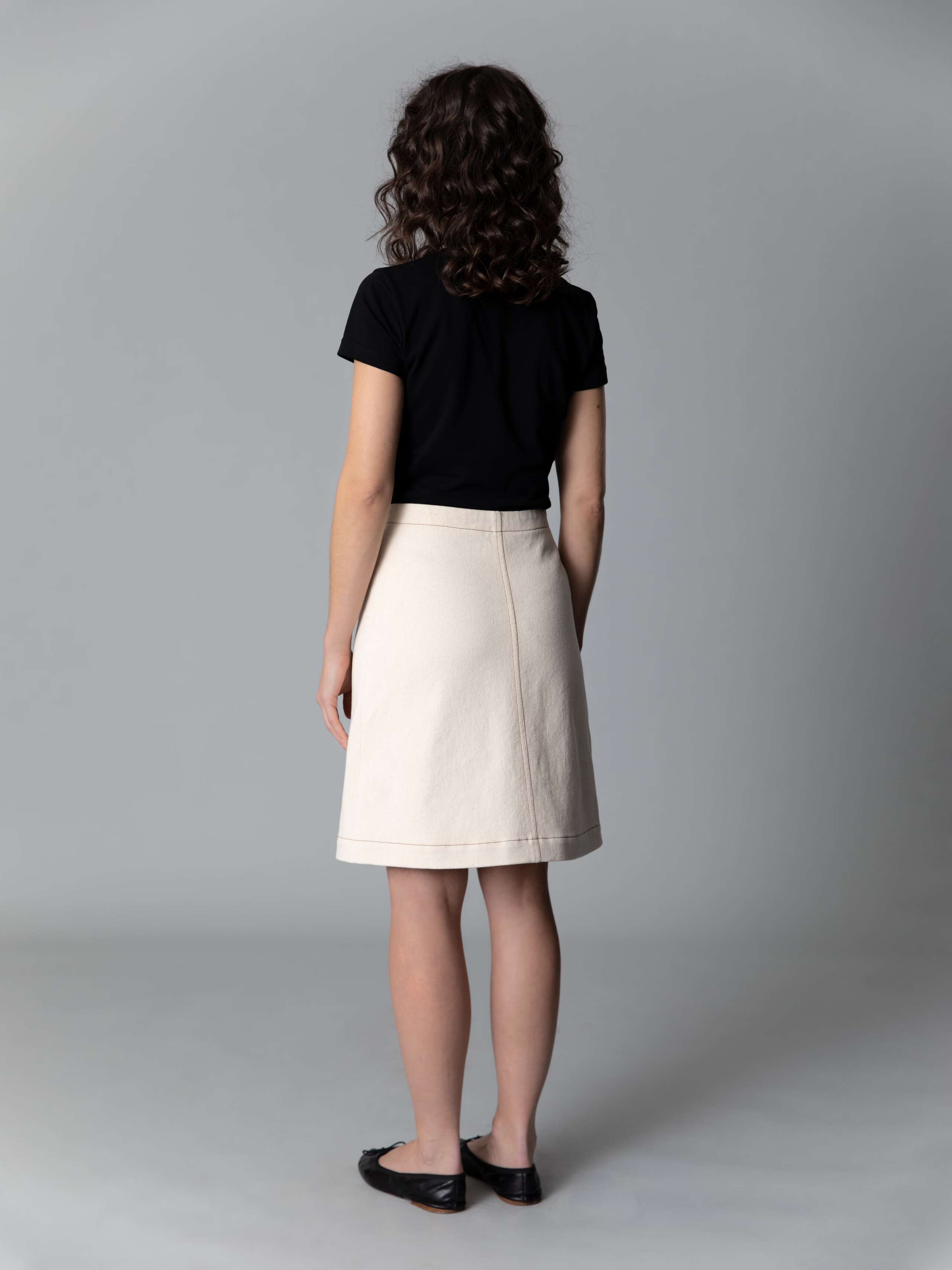 Model wears a beautiful a-line denim skirt in an ecru colour shade combined with black ballerina flats and a black t-shirt
