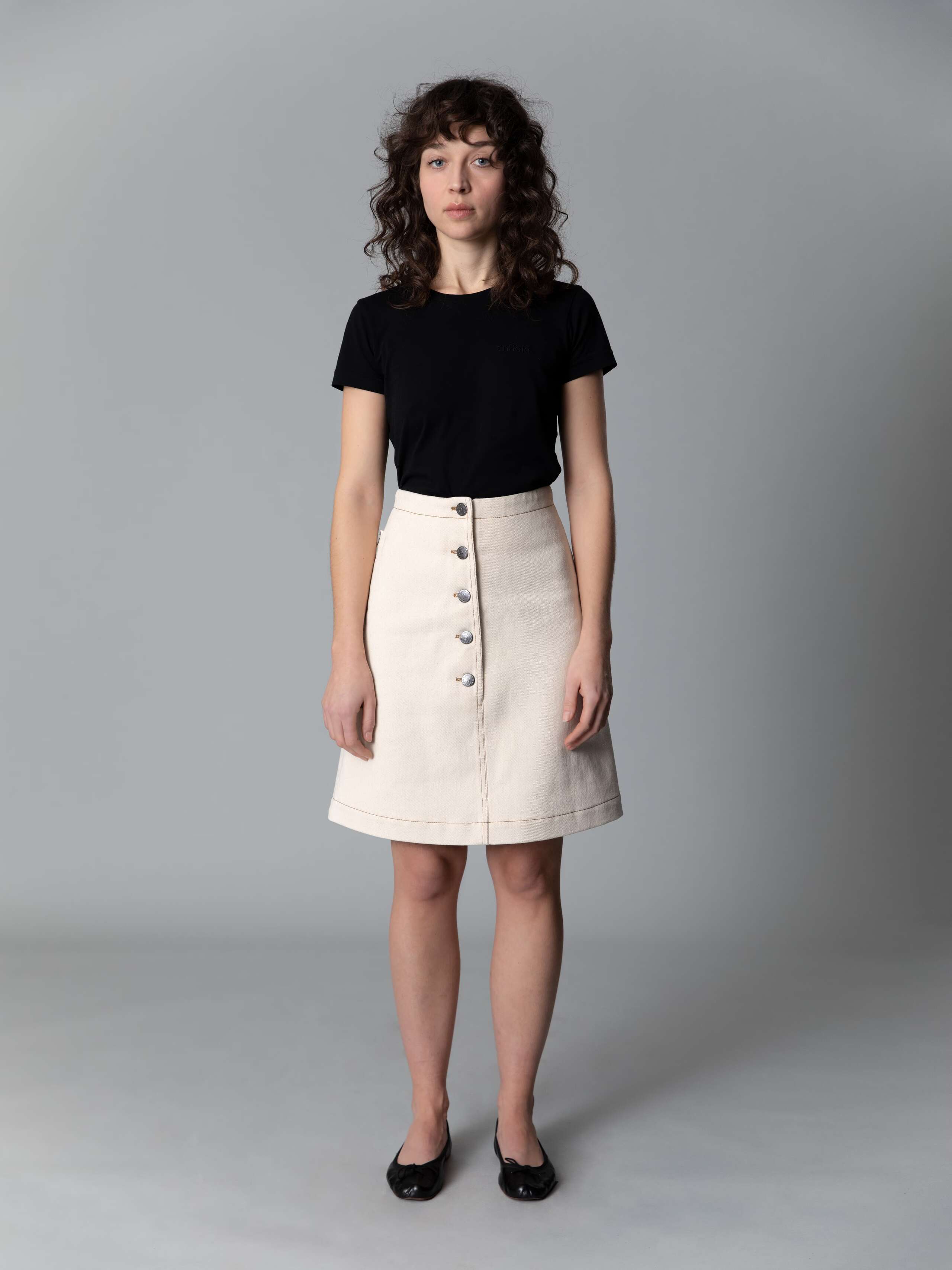 Model wears a beautiful a-line denim skirt in an ecru colour shade combined with black ballerina flats and a black t-shirt