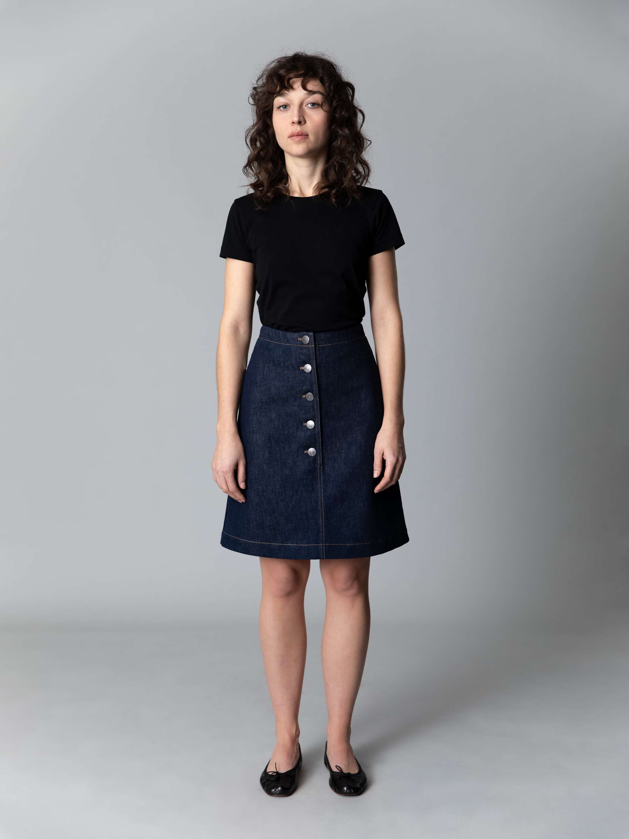 Model is wearing a beautiful a-line denim skirt combined with a black shirt and black ballerina flats