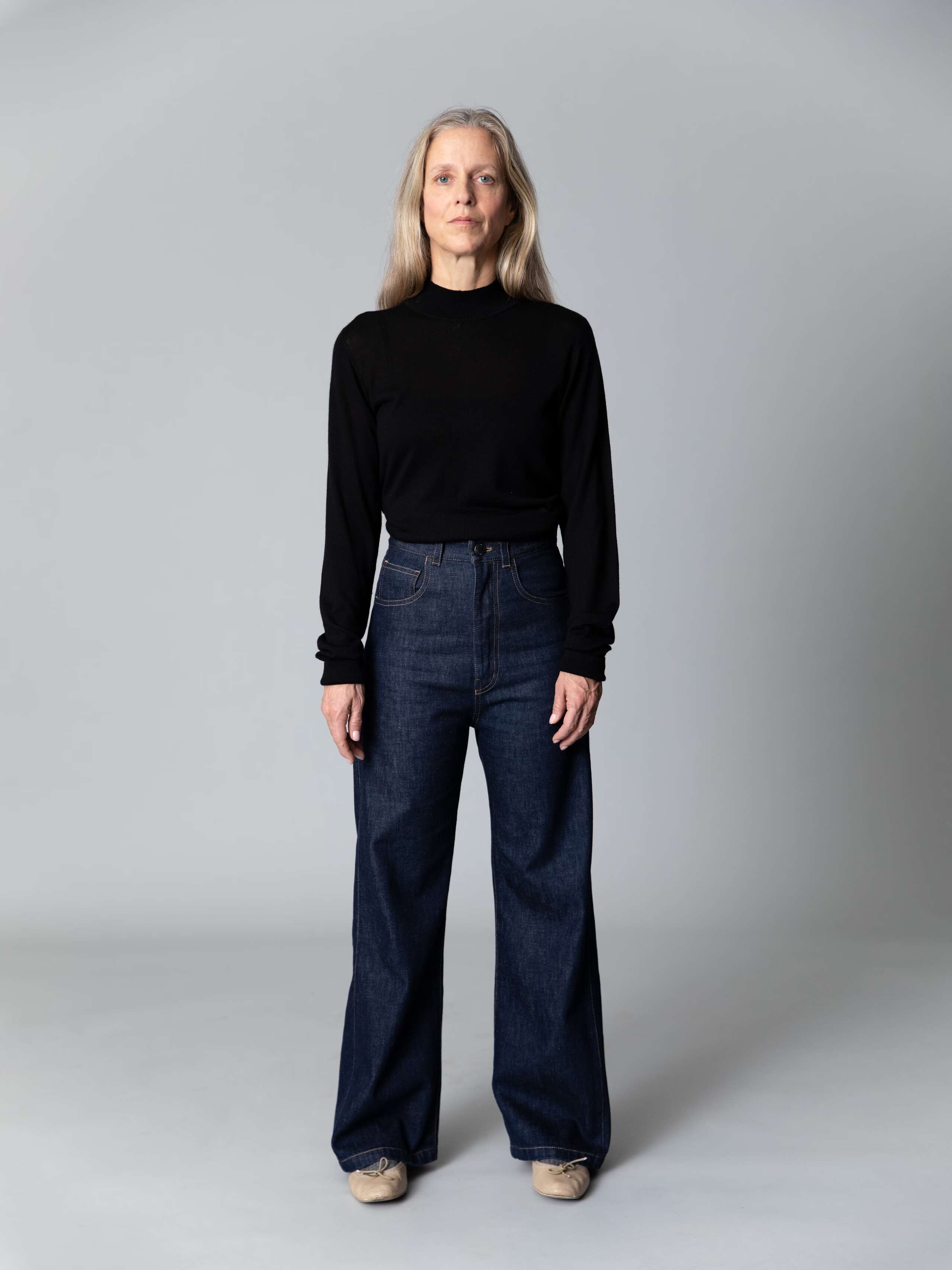 Model with blond hair and light blue eyes wears a black turtleneck pullover and a beuatiful wide leg jeans in dark pure indigo 