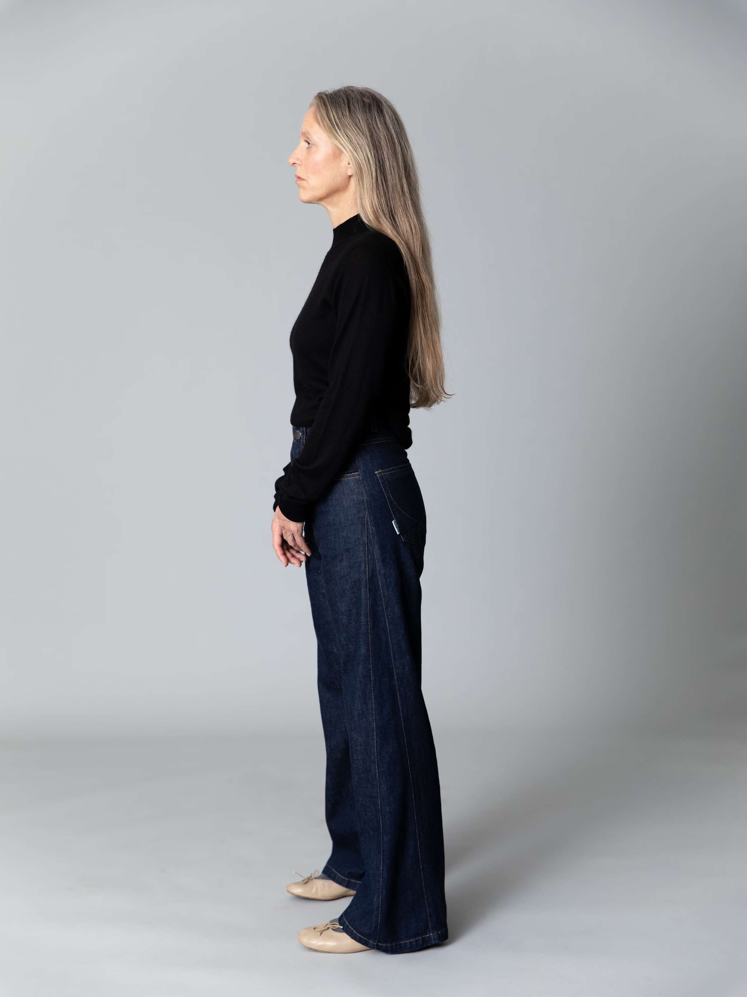 Model with blond hair and light blue eyes wears a black turtleneck pullover and a beuatiful wide leg jeans in dark pure indigo 