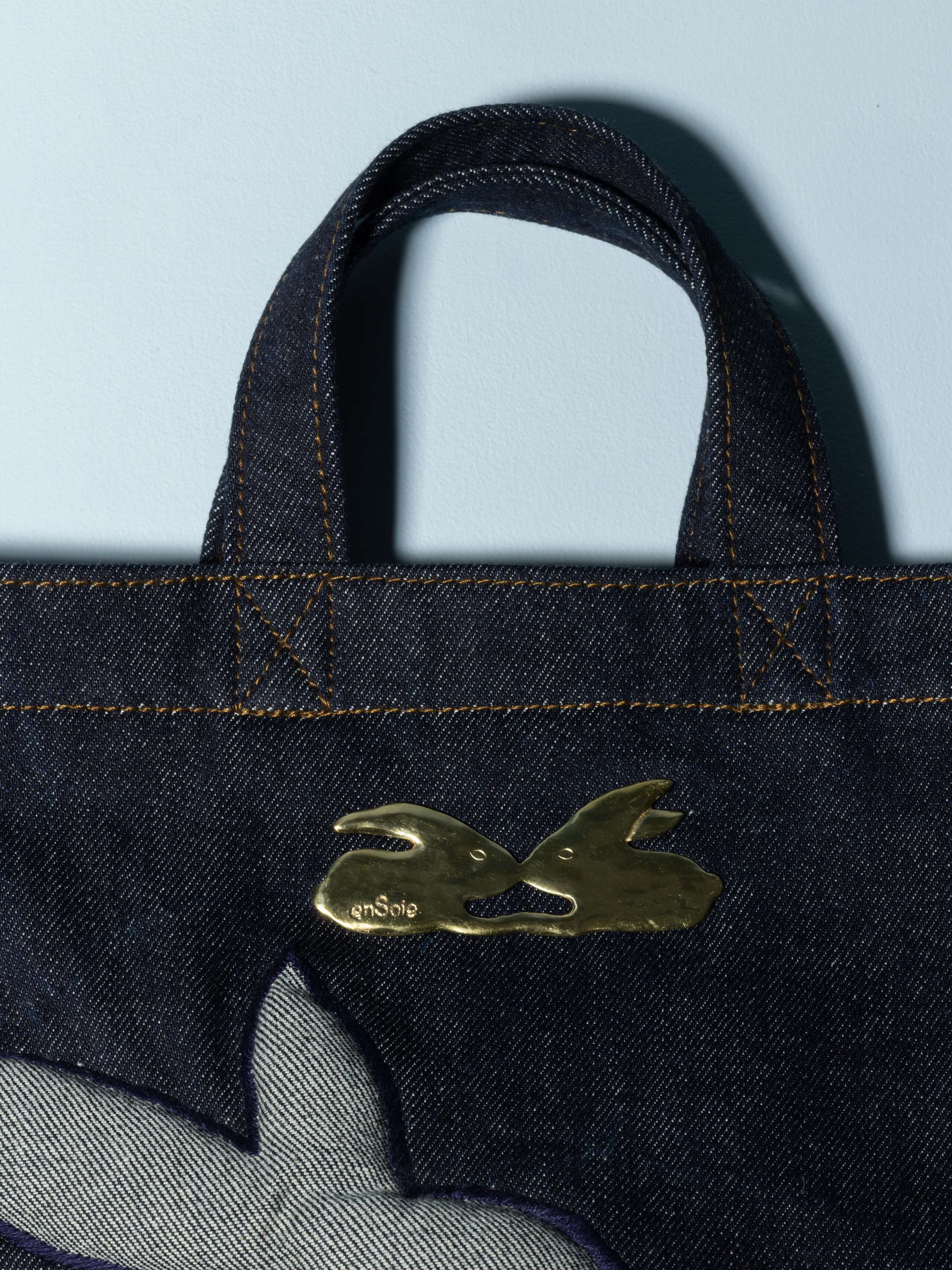 Detail of a denim bag with rabbut application in a beautiful indigo blue feauturing a beautiful rabbit brass tag