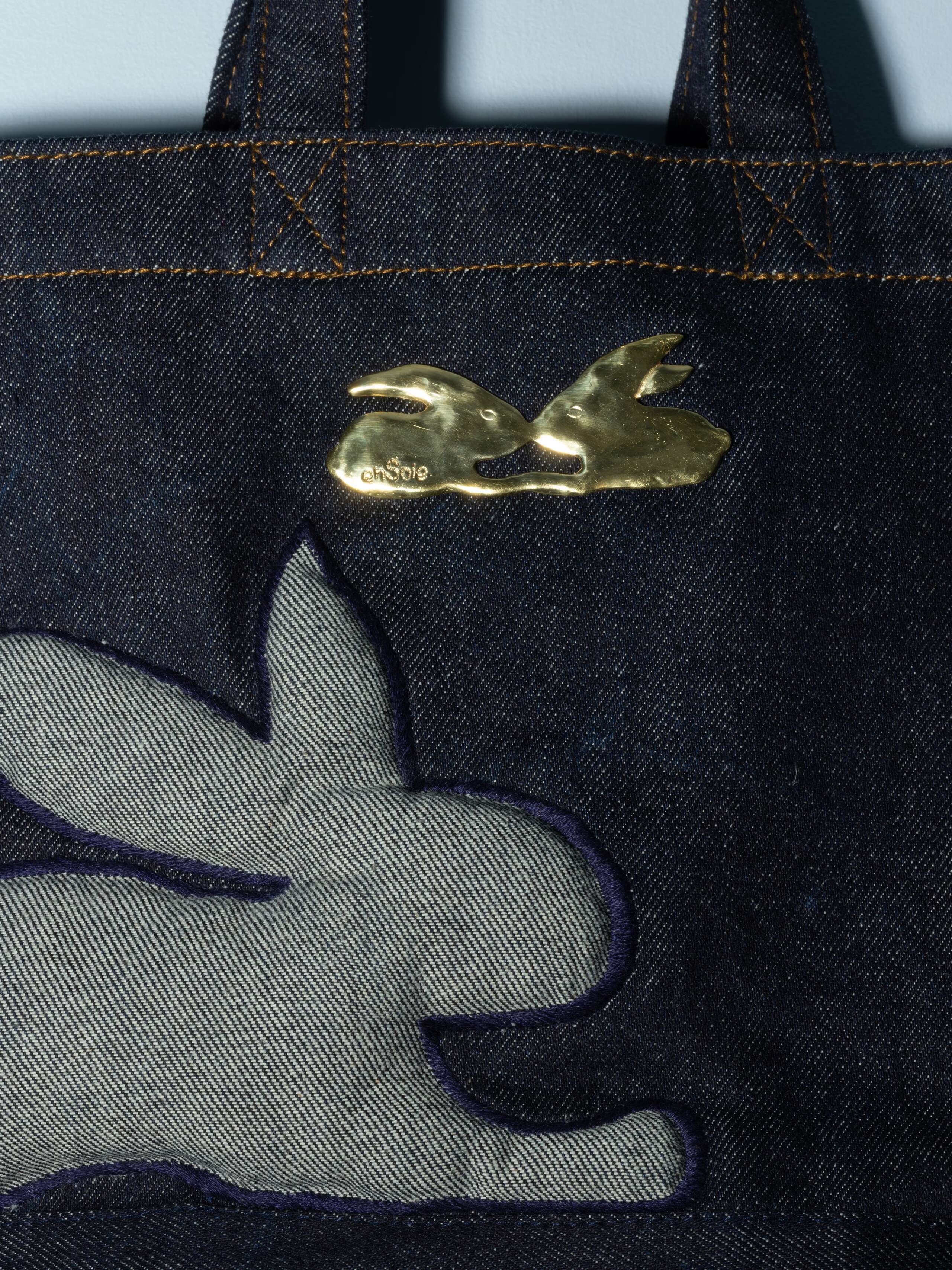 Detail of a denim bag with rabbut application in a beautiful indigo blue feauturing a beautiful rabbit brass tag