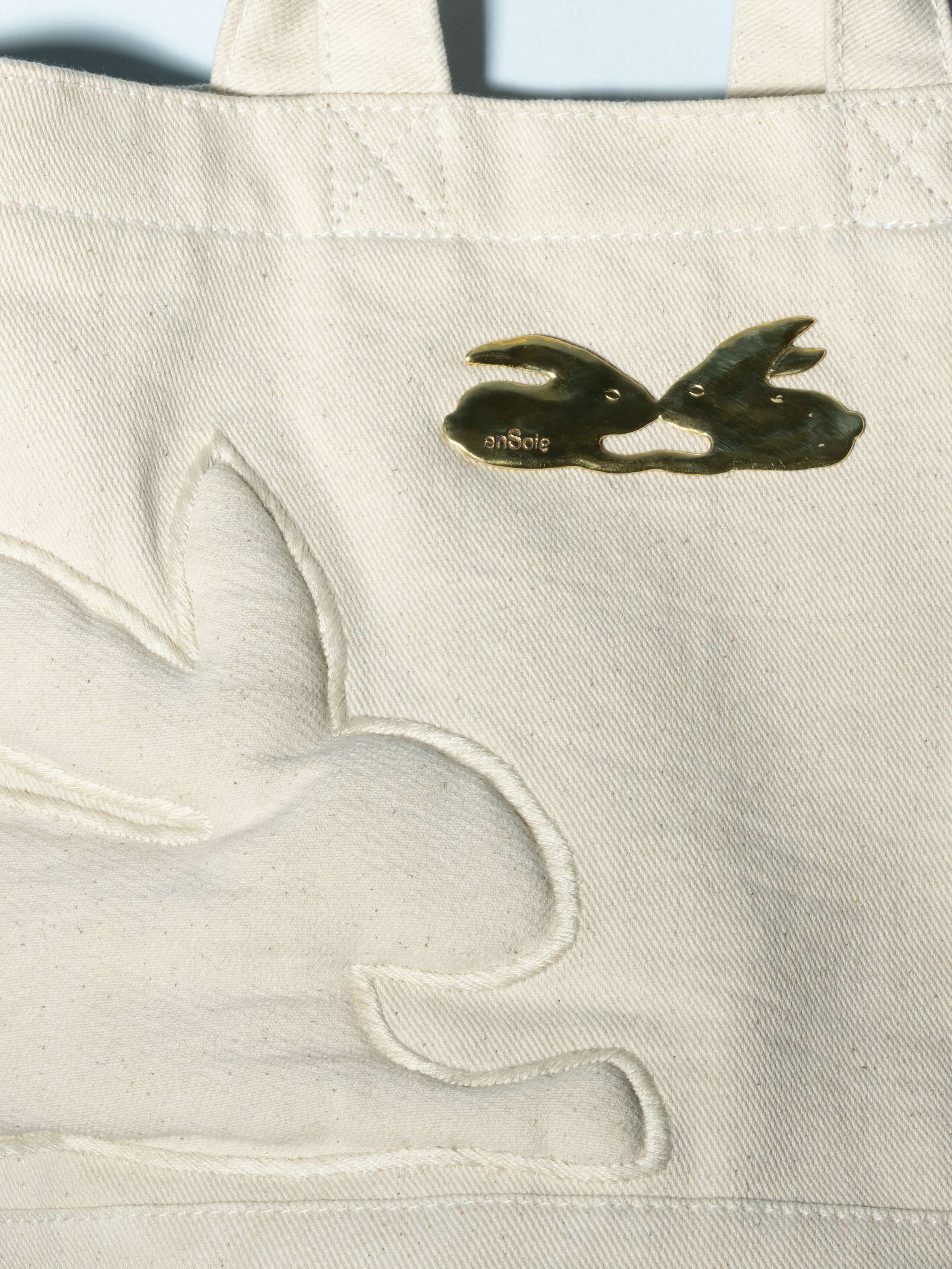 Detail of a denim bag with rabbut application in a beautiful ecru white feauturing a beautiful rabbit brass tag