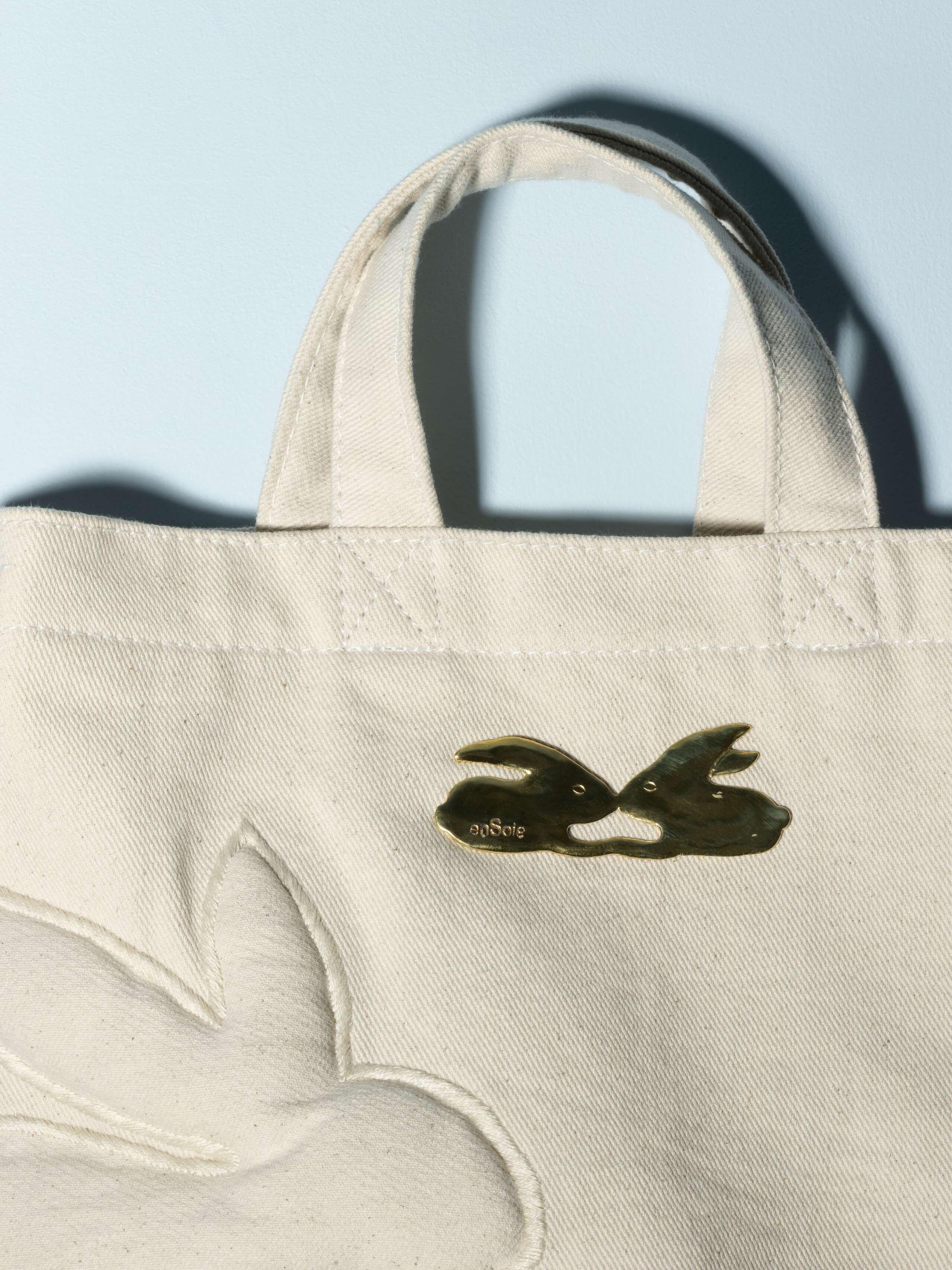 Detail of a denim bag with rabbut application in a beautiful ecru white feauturing a beautiful rabbit brass tag