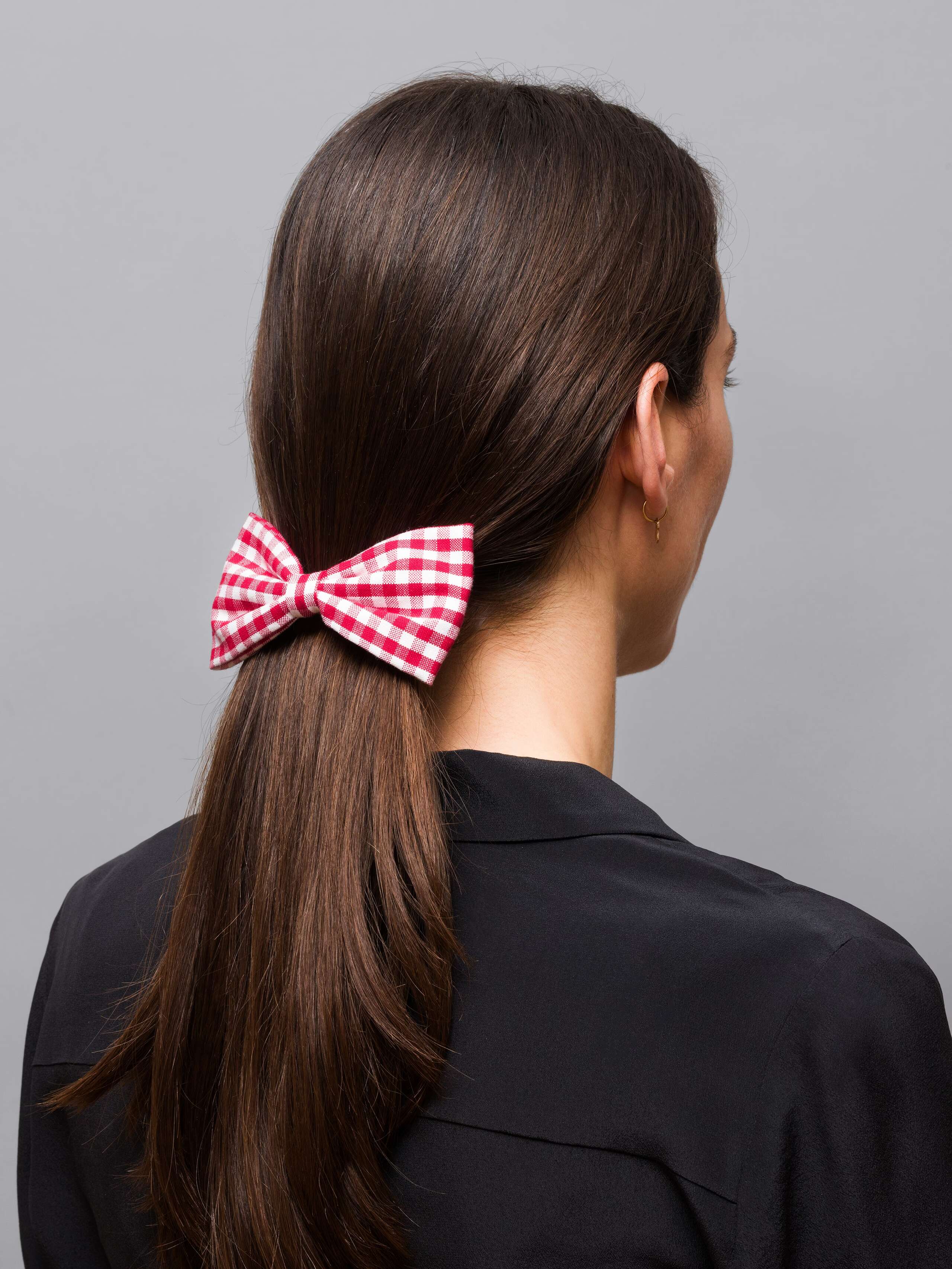 Picture of a women with dark brown hair wearing a bow hair clip made of red vichy check pattern
