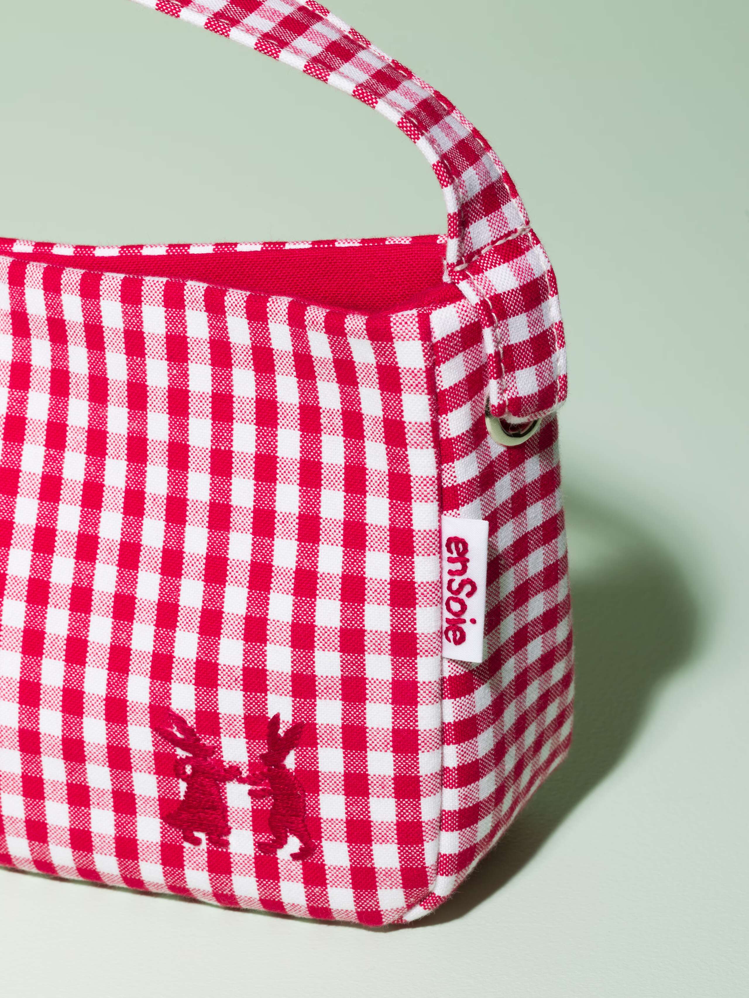 Detail of a small baguette bag made of cotton featuring a red vichy check pattern