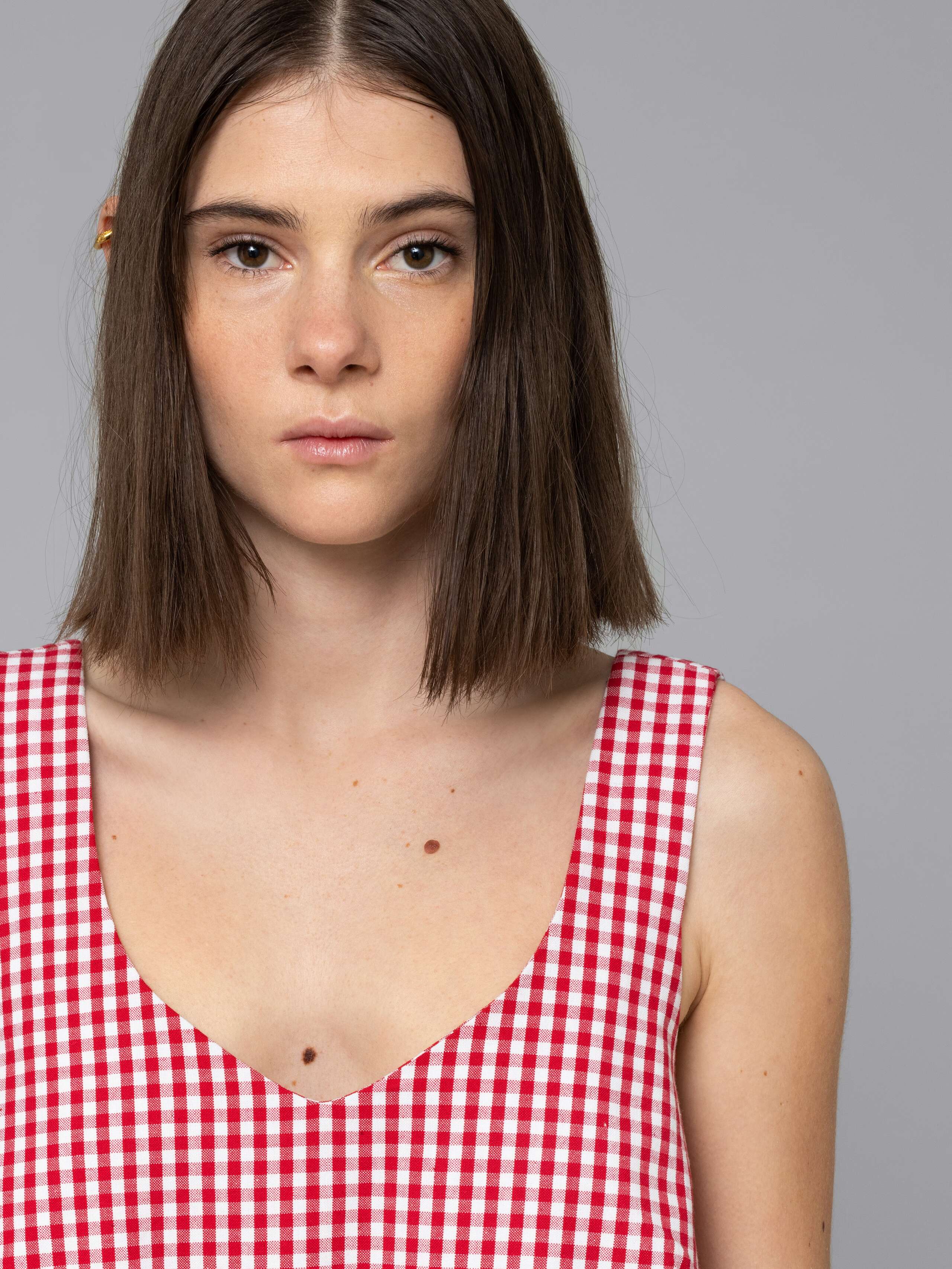 Female model is wearing an airy cotton dress featuring a red vichy check pattern