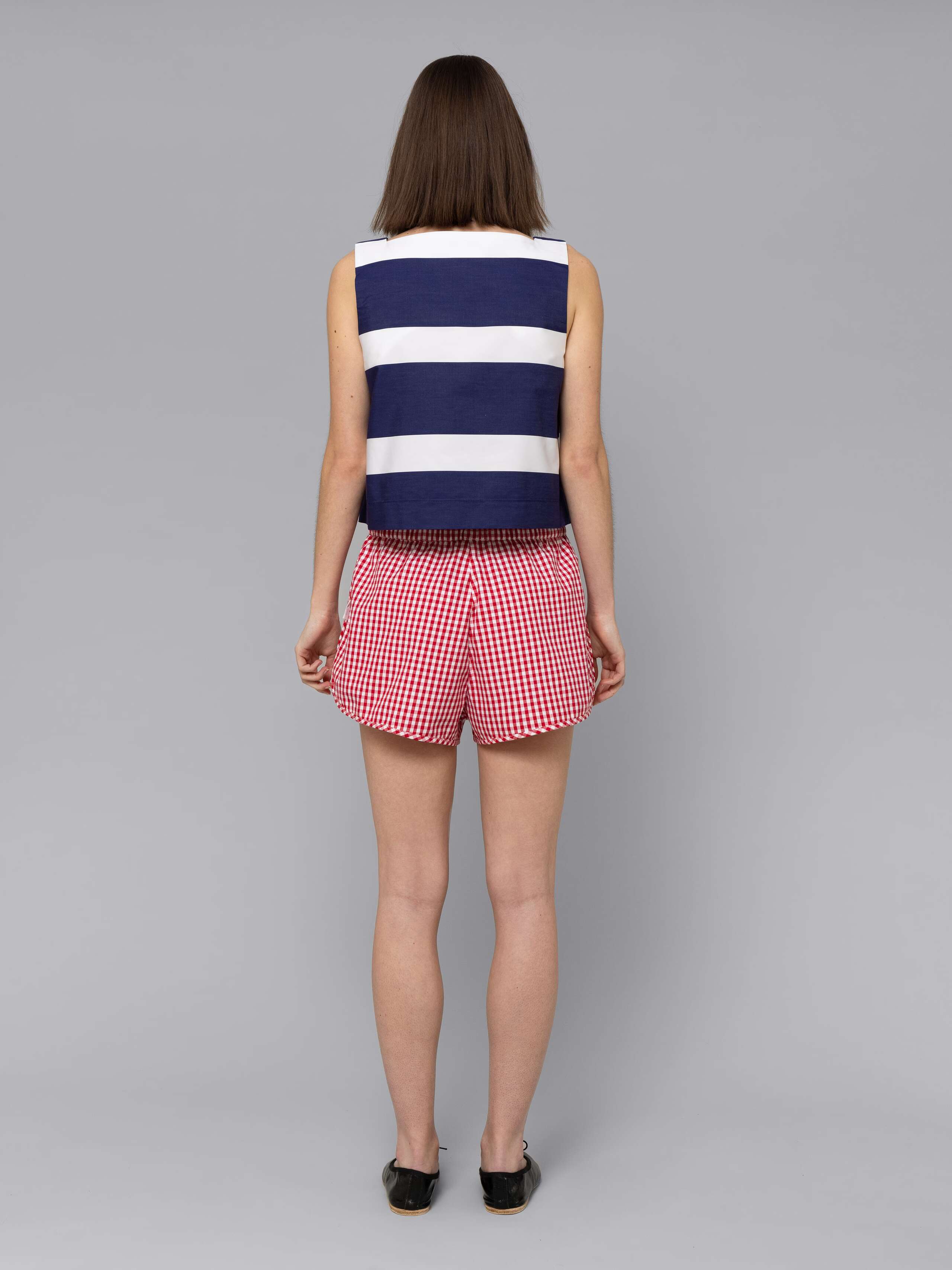 Female model is wearing a sporty cotton short featuring a red vichy check pattern