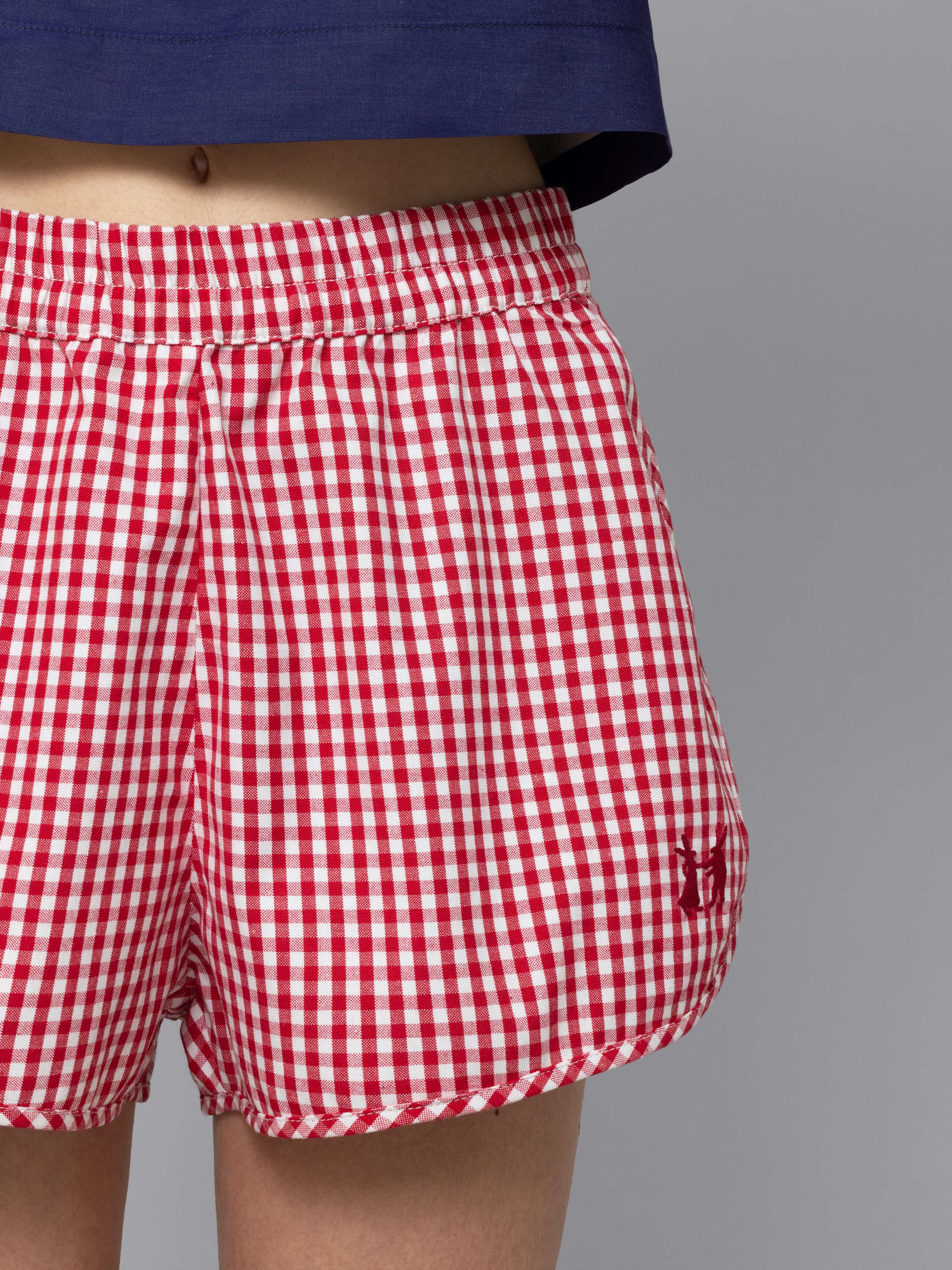 Female model is wearing a sporty cotton short featuring a red vichy check pattern