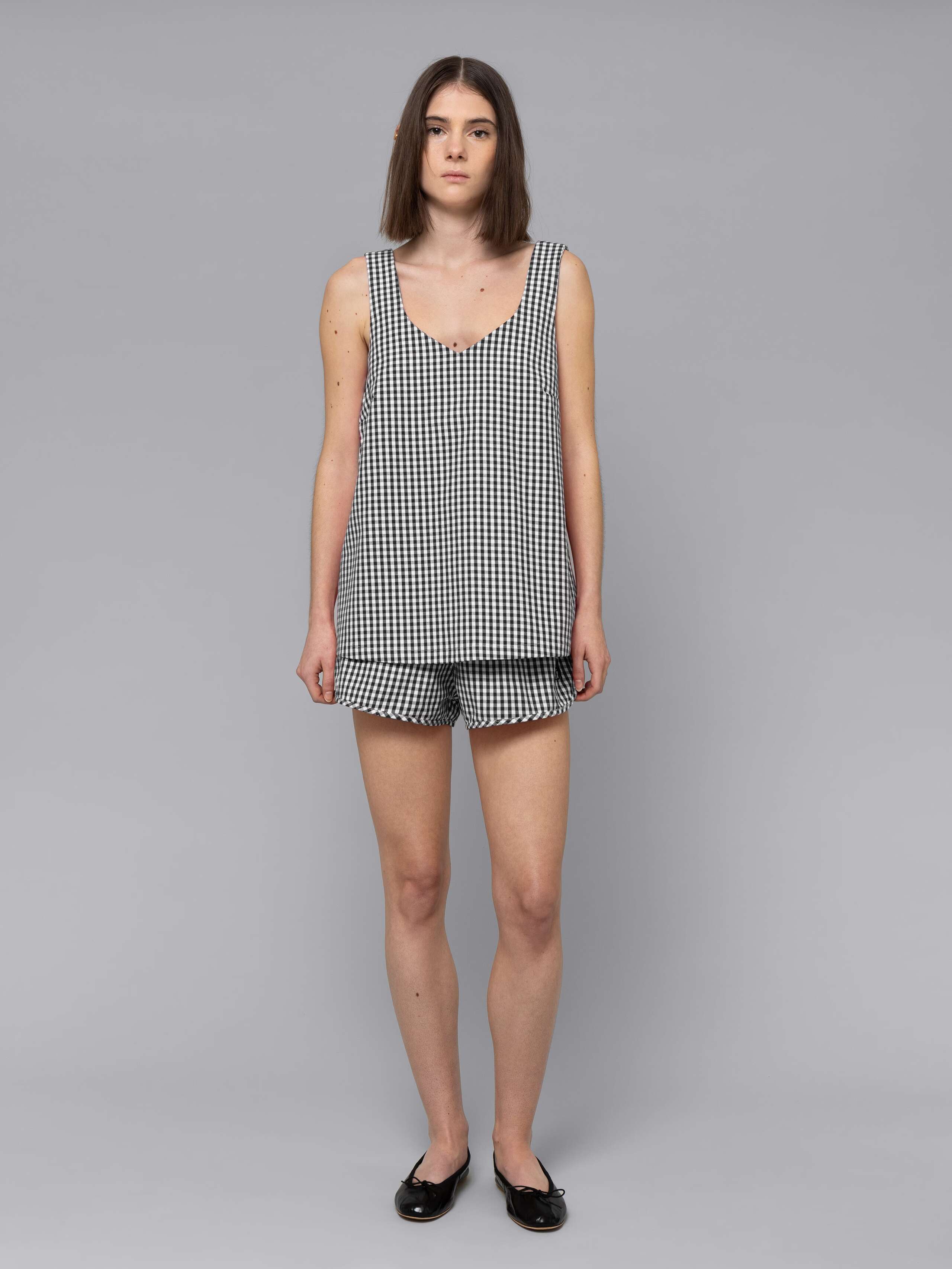 Female model is wearing a combination of a long airy cotton top and a sporty cotton short featuring a beautiful black vichy check pattern