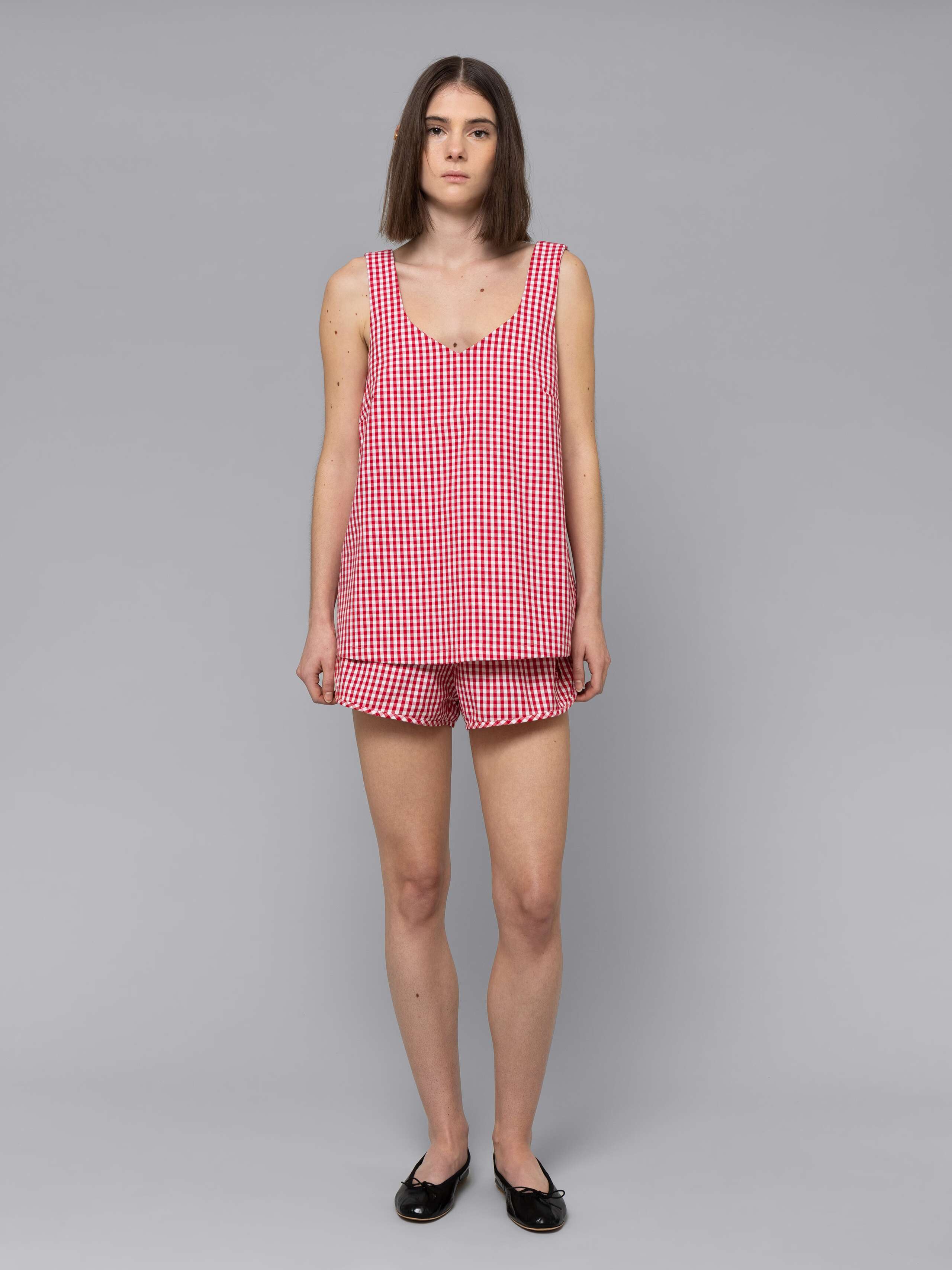 Female model is wearing a combination of a long airy cotton top and a sporty cotton short featuring a beautiful red vichy check pattern