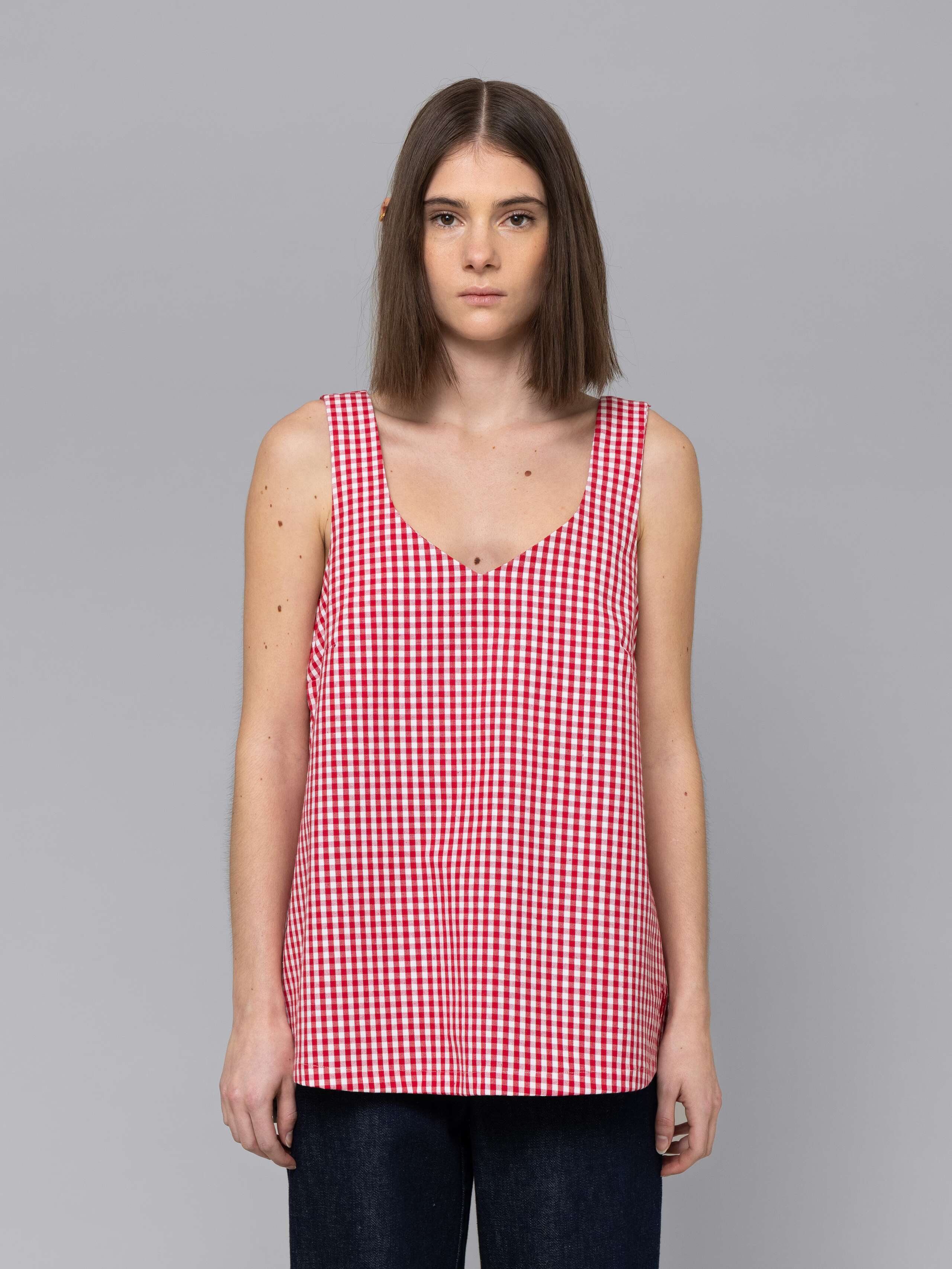 Female model is wearing a an airy long top featuring a beautiful red vichy check pattern