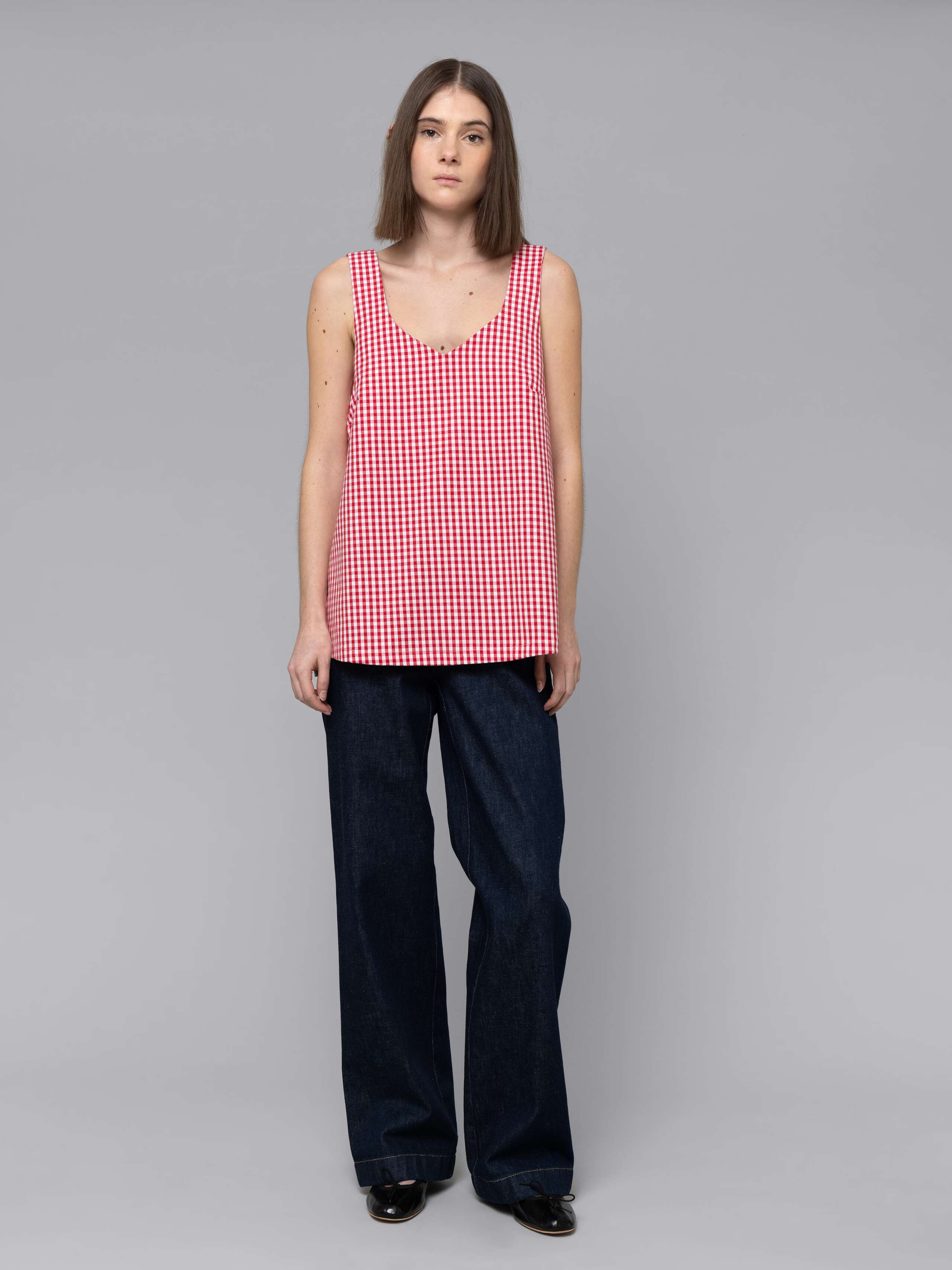 Female model is wearing a an airy long top featuring a beautiful red vichy check pattern