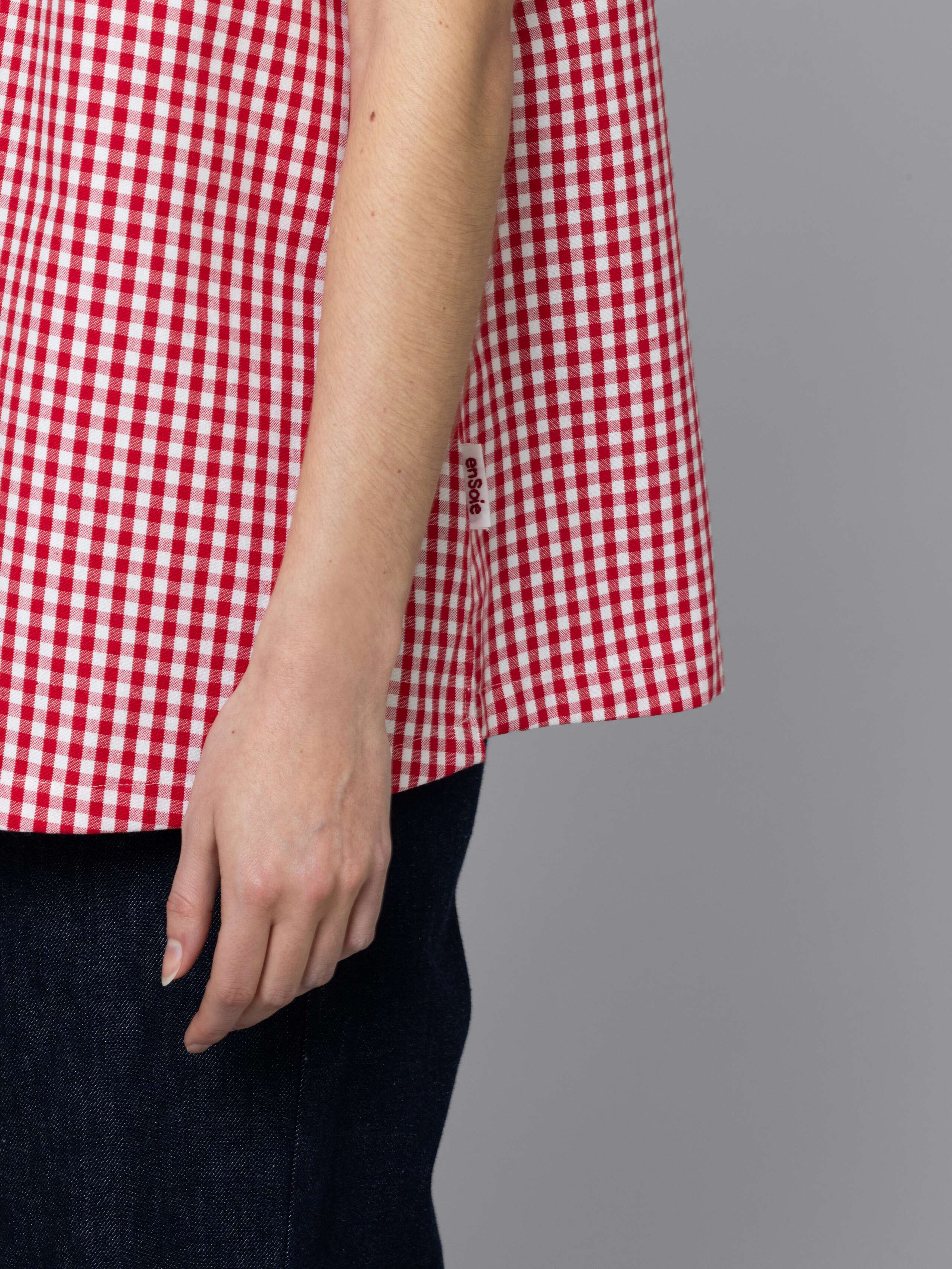Female model is wearing a an airy long top featuring a beautiful red vichy check pattern