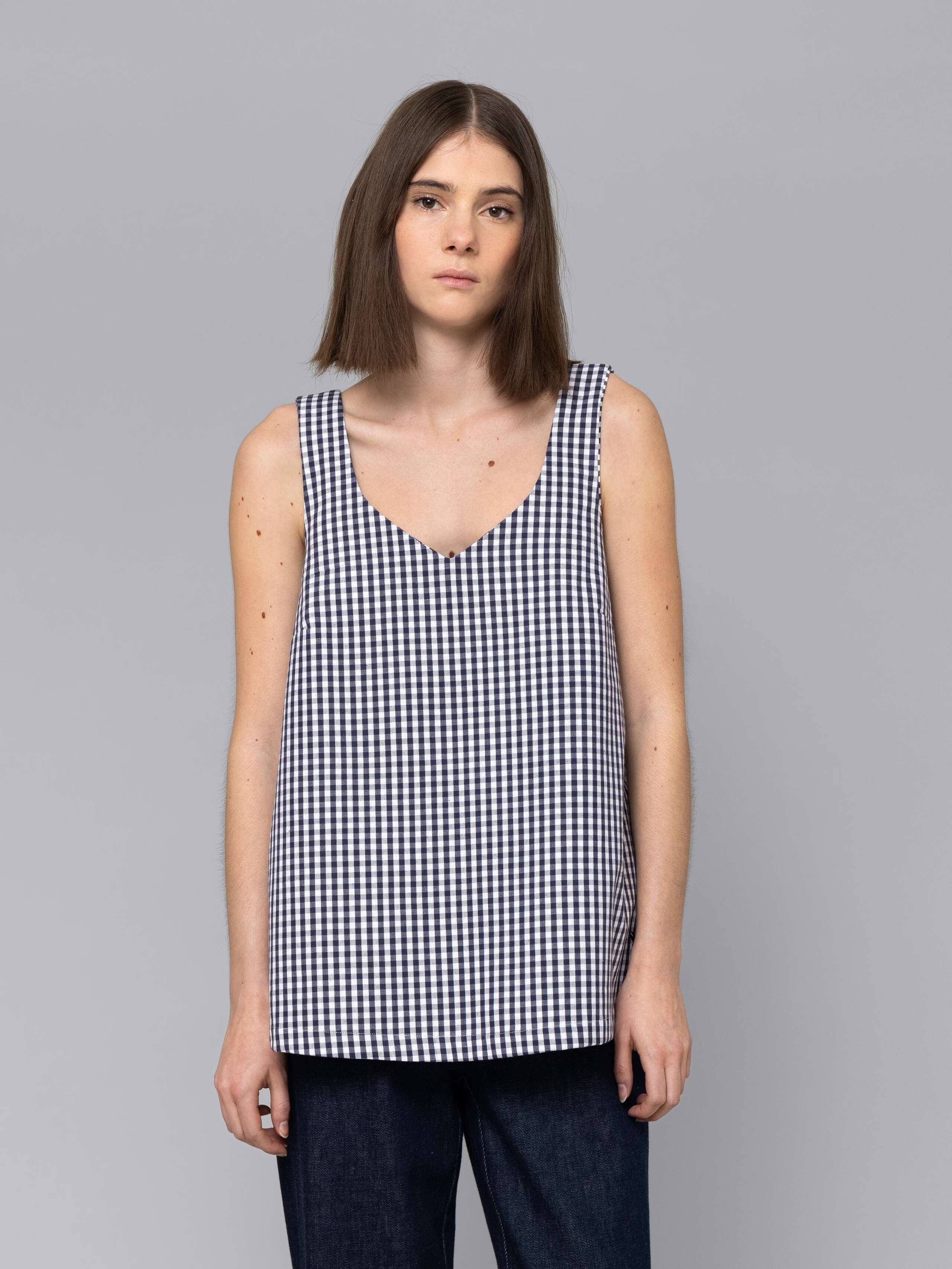 Female model is wearing a an airy long top featuring a beautiful navy vichy check pattern