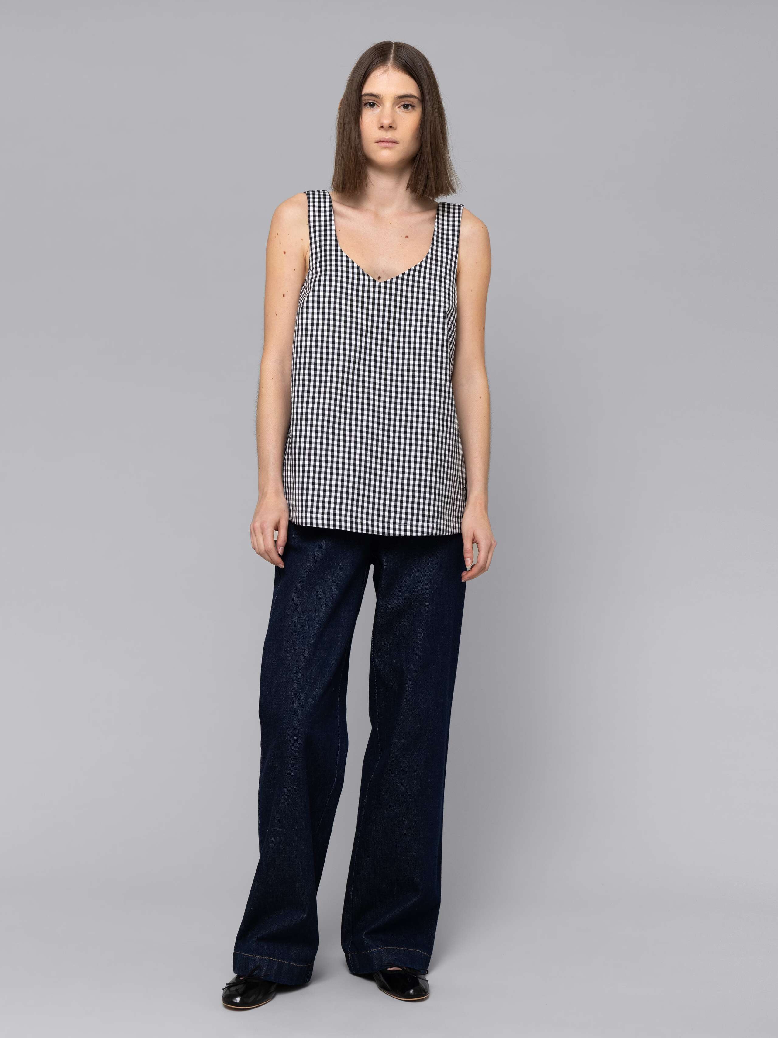 Female model is wearing a an airy long top featuring a beautiful black vichy check pattern