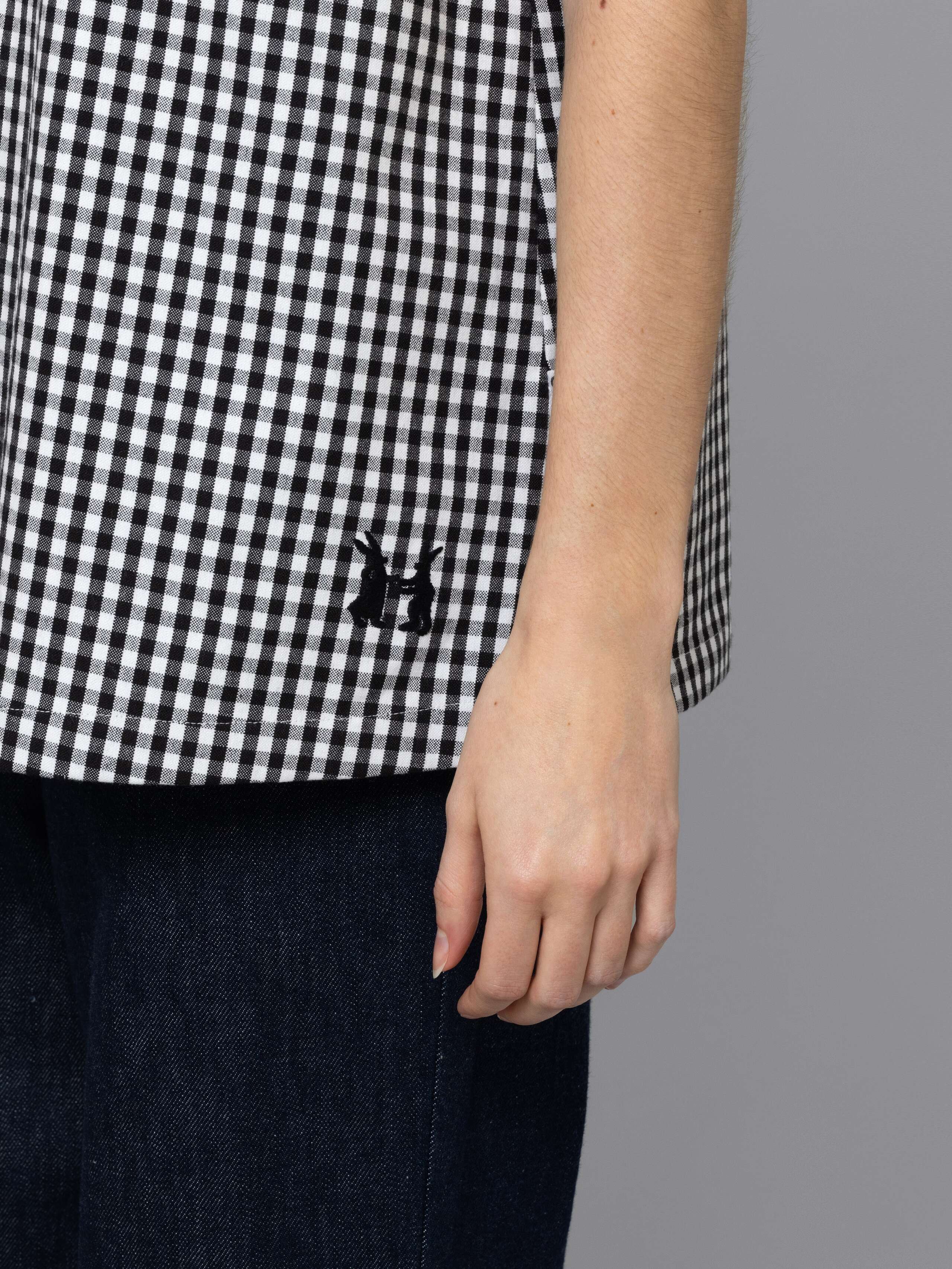 Female model is wearing a an airy long top featuring a beautiful black vichy check pattern