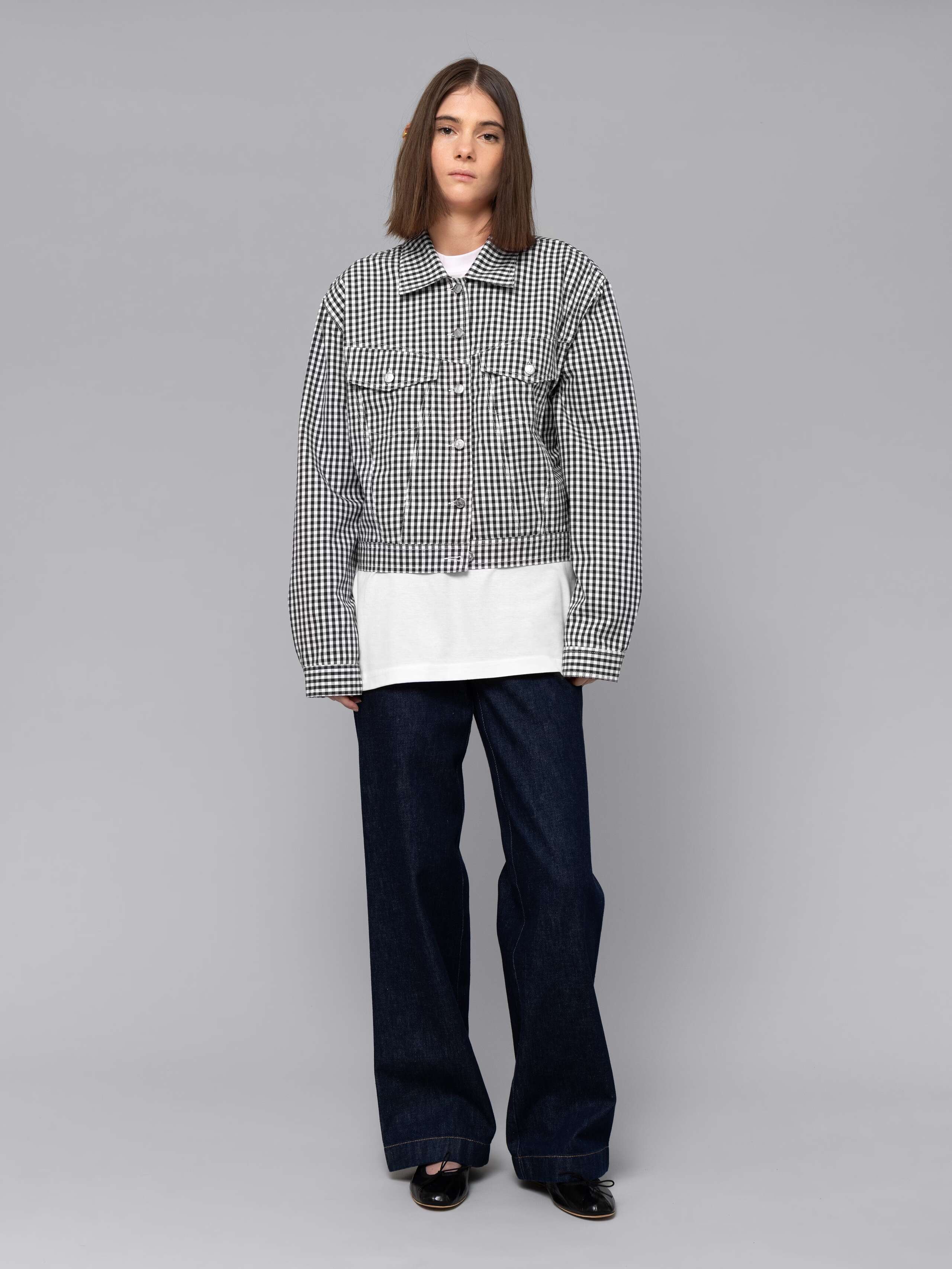 Female model is wearing a a boxy denim trucker jacket featuring a beautiful black vichy check pattern