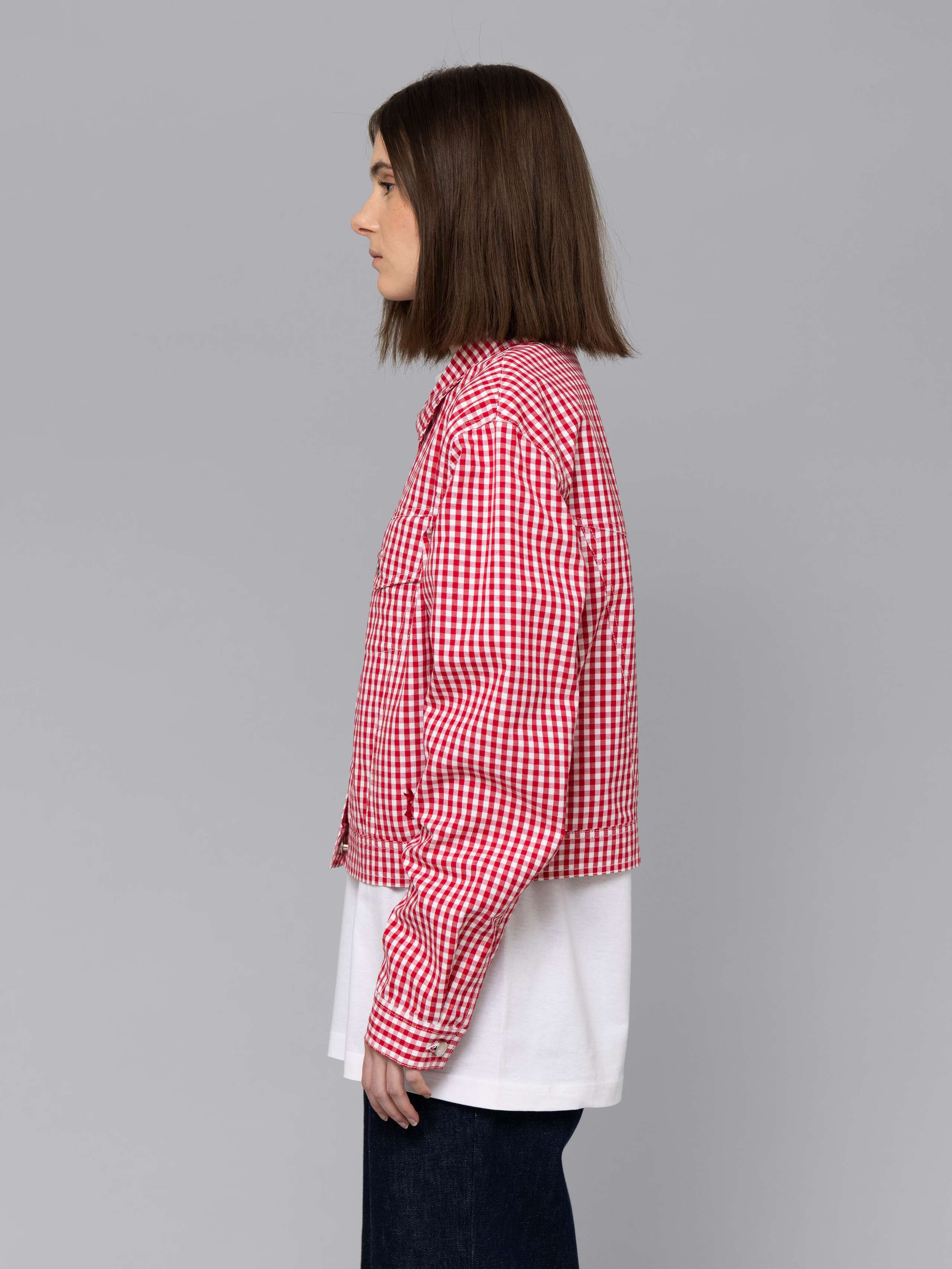 Female model is wearing a a boxy denim trucker jacket featuring a beautiful red vichy check pattern