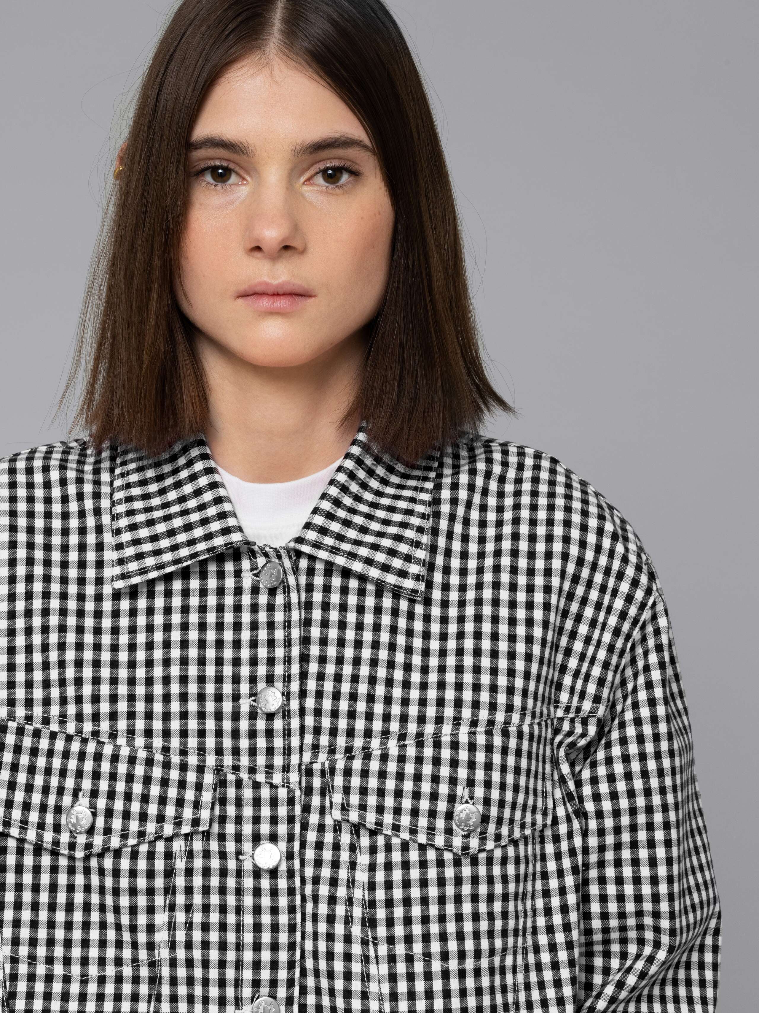 Female model is wearing a a boxy denim trucker jacket featuring a beautiful black vichy check pattern