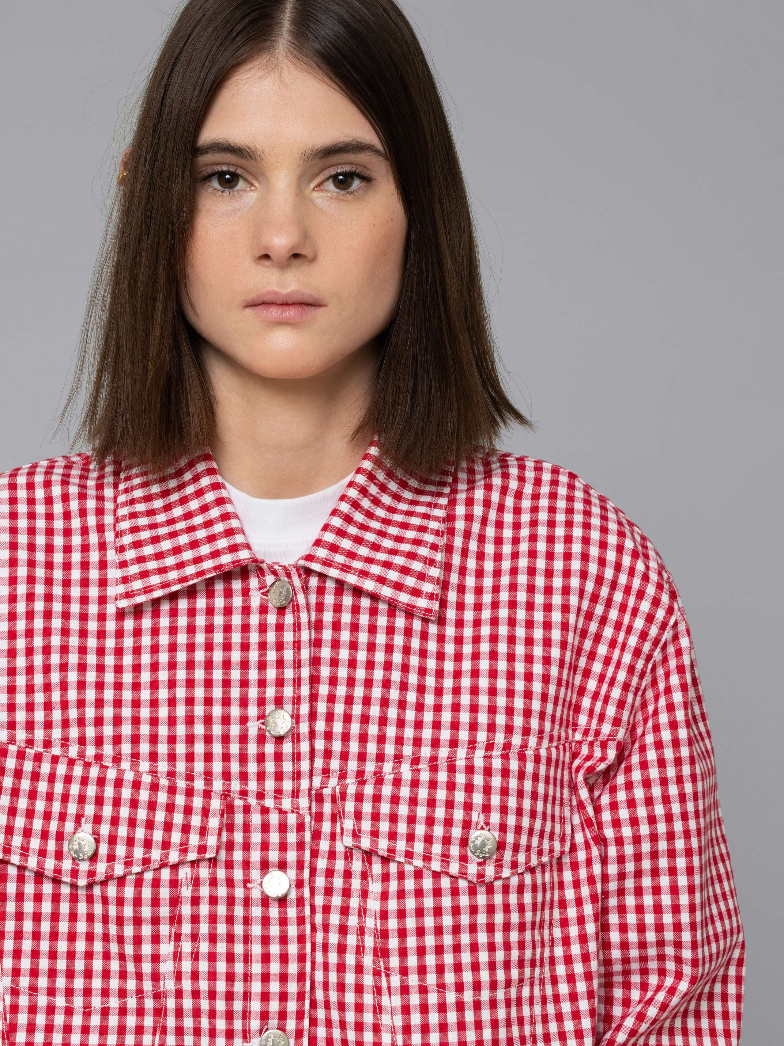 Female model is wearing a a boxy denim trucker jacket featuring a beautiful red vichy check pattern