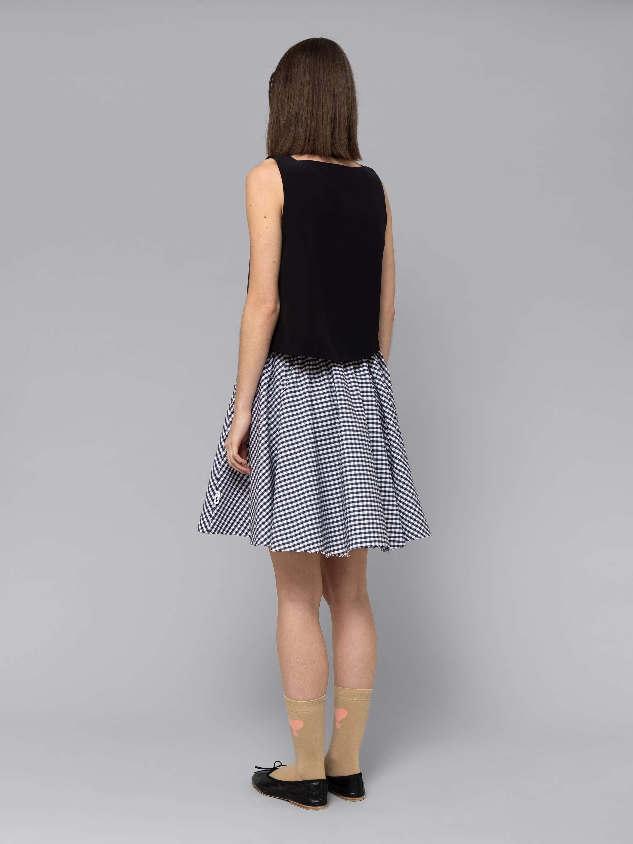 Female model is wearing a combination of a boxy black silk top and a cute short cotton skirt  featuring a beautiful navy vichy check pattern