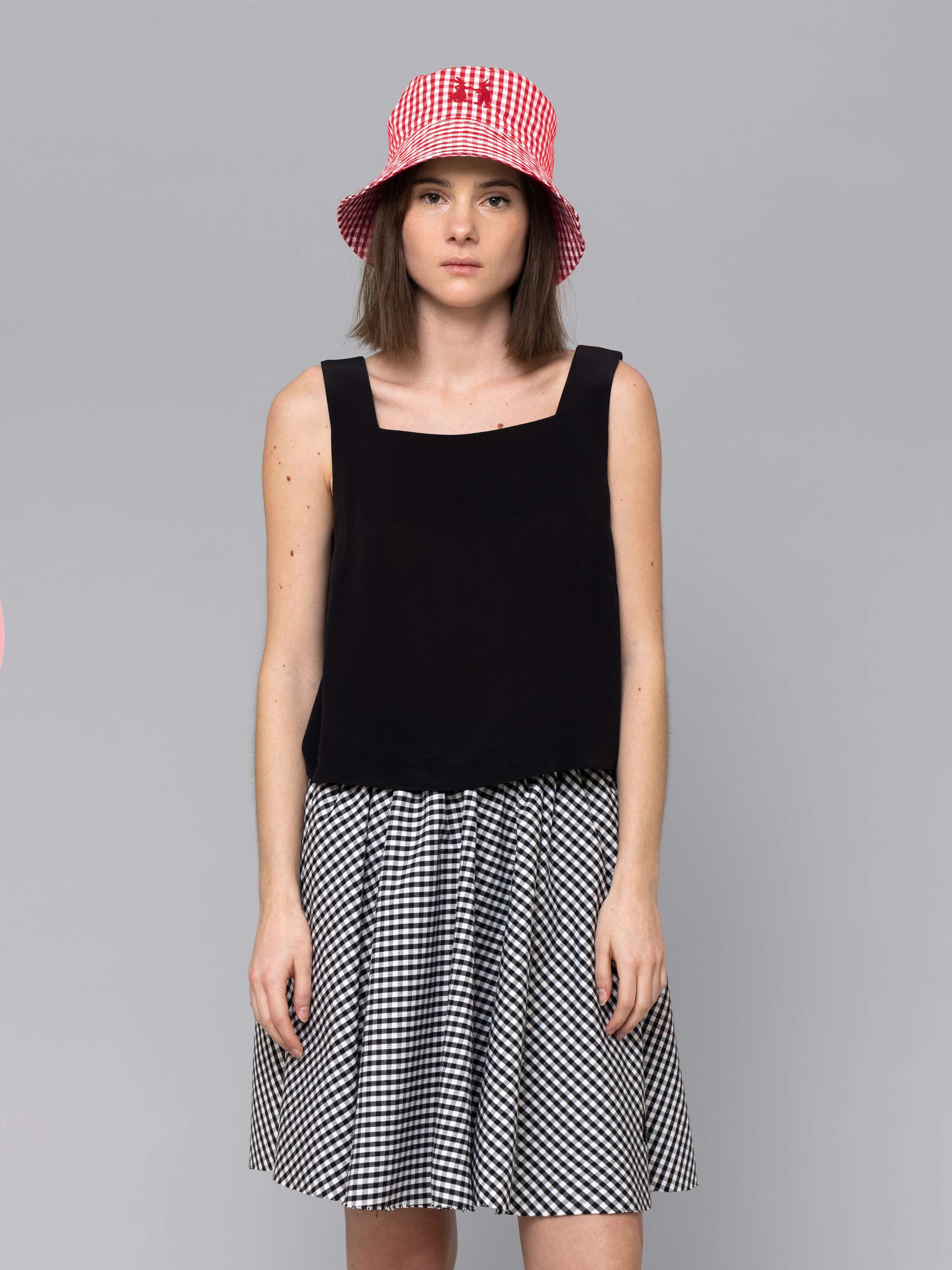 Female model is wearing a combination of a boxy black silk top and a cute short cotton skirt  featuring a beautiful black vichy check pattern