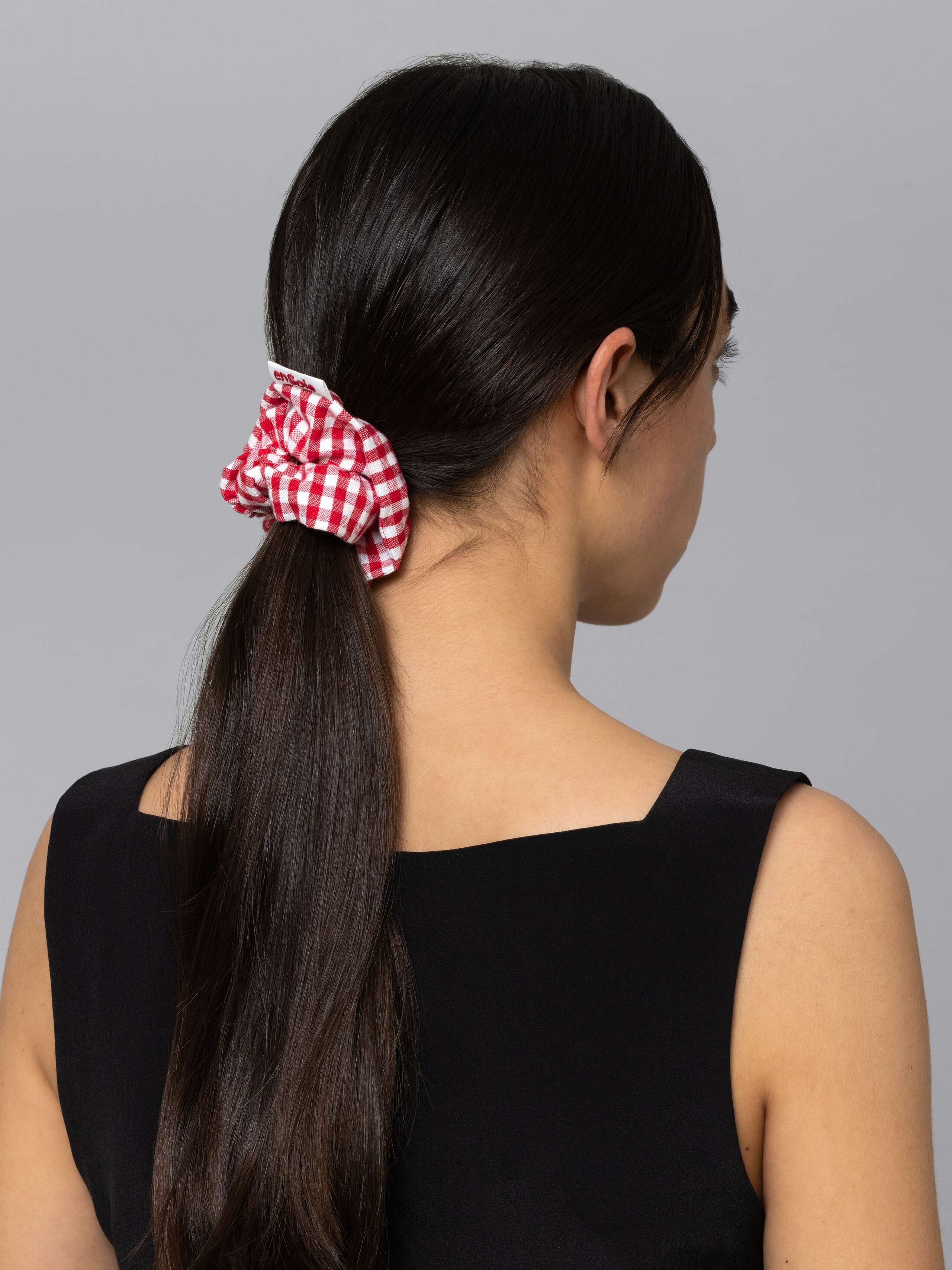 Picture of a women with dark brown hair wearing a cotton scrunchie featuring a red vichy check pattern 