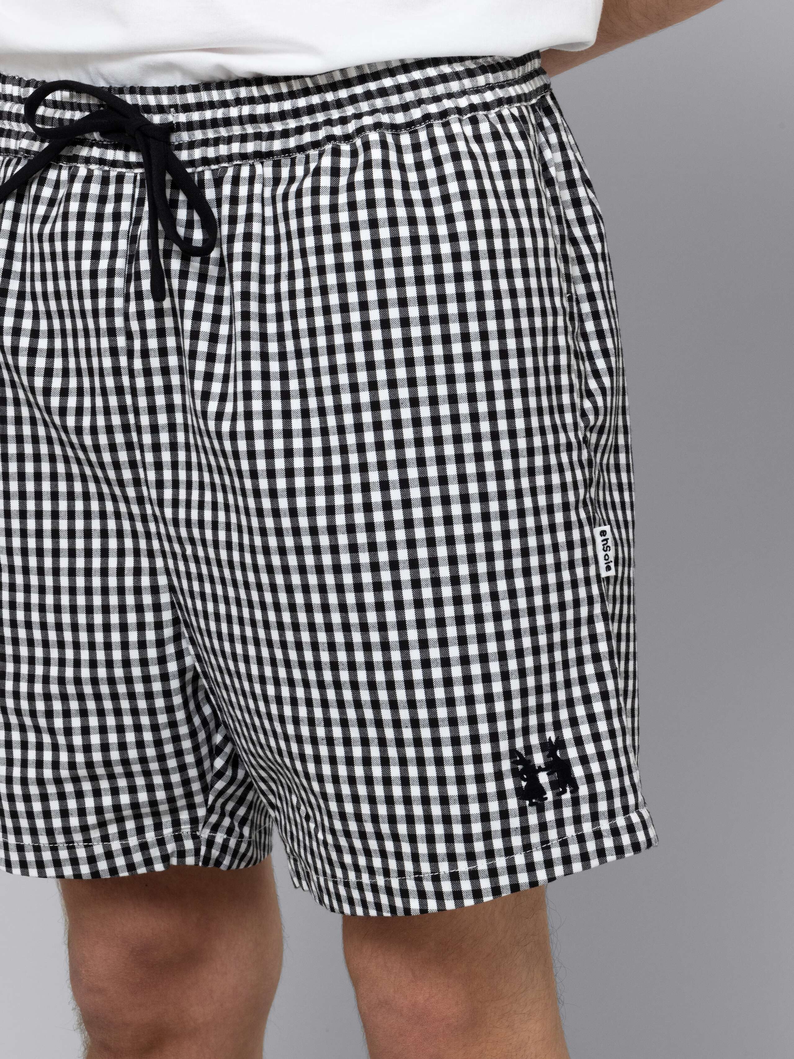 Male model is wearing a summery combination of a cotton short featuring a black vichy check pattern and a white t-shirt