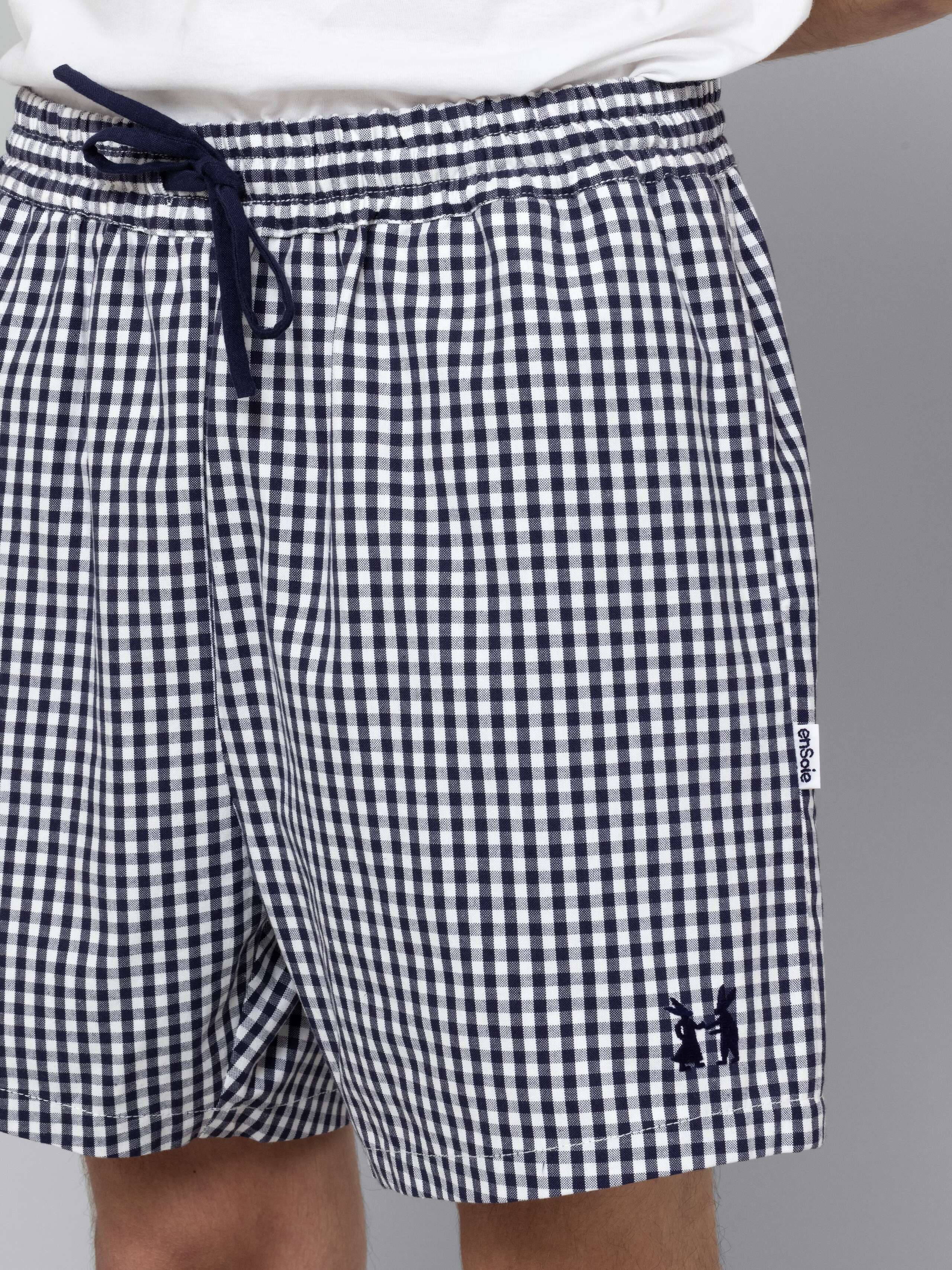 Male model is wearing a summery combination of a cotton short featuring a navy vichy check pattern and a white t-shirt