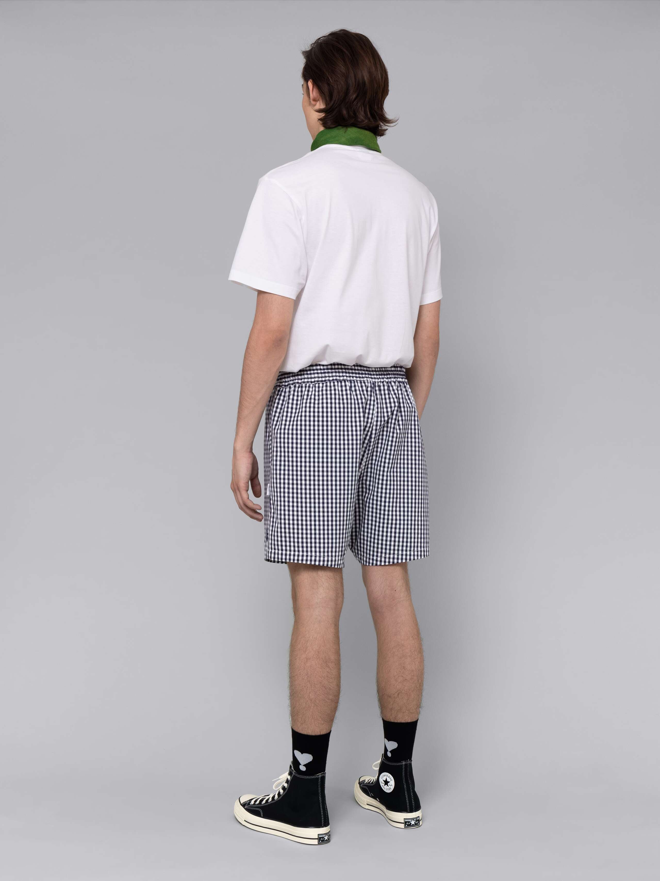 Male model is wearing a summery combination of a cotton short featuring a navy vichy check pattern and a white t-shirt