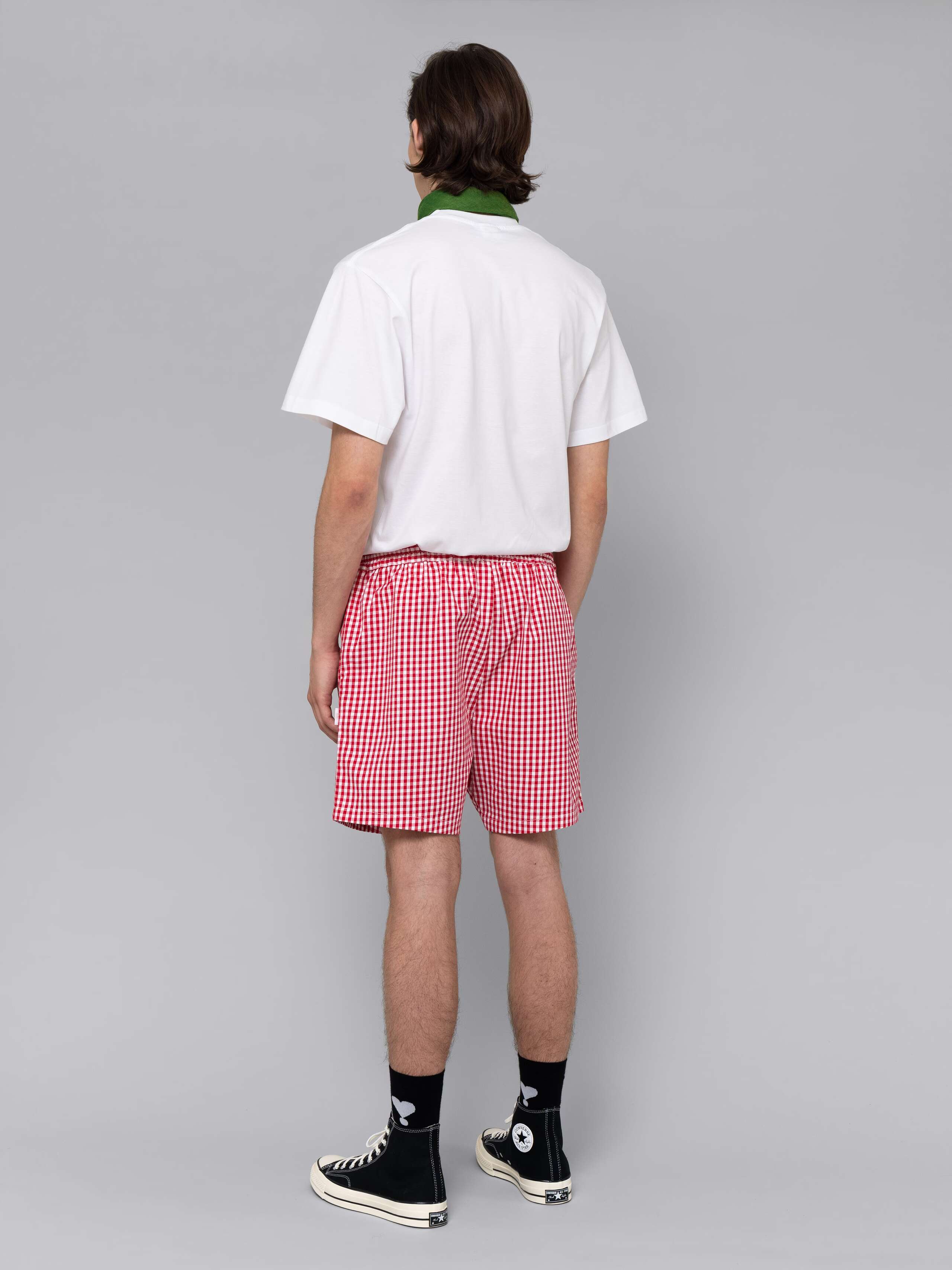 Male model is wearing a summery combination of a cotton short featuring a red vichy check pattern and a white t-shirt
