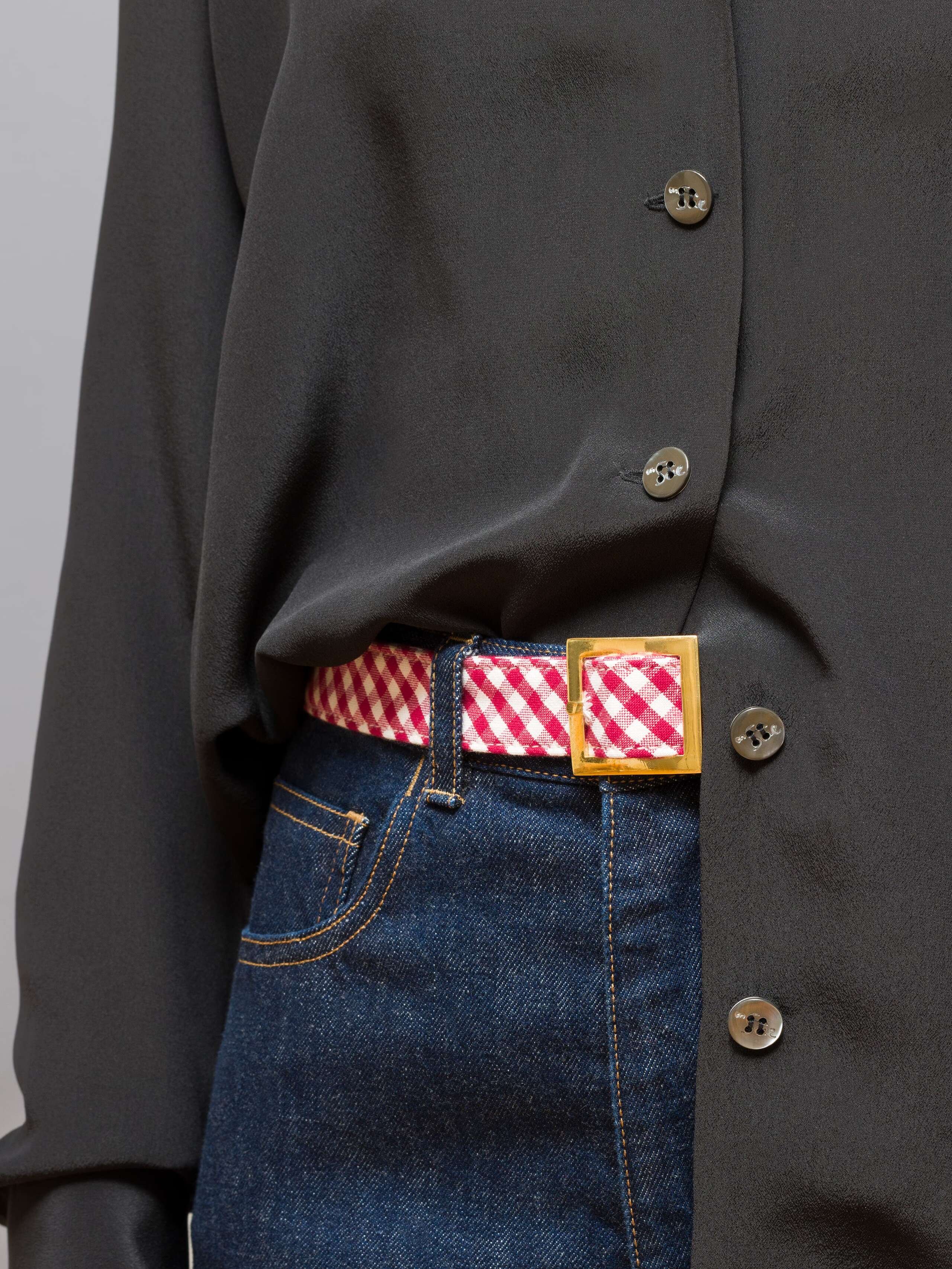 Picture of a detail of a belt made of cotton featuring a red vichy check pattern