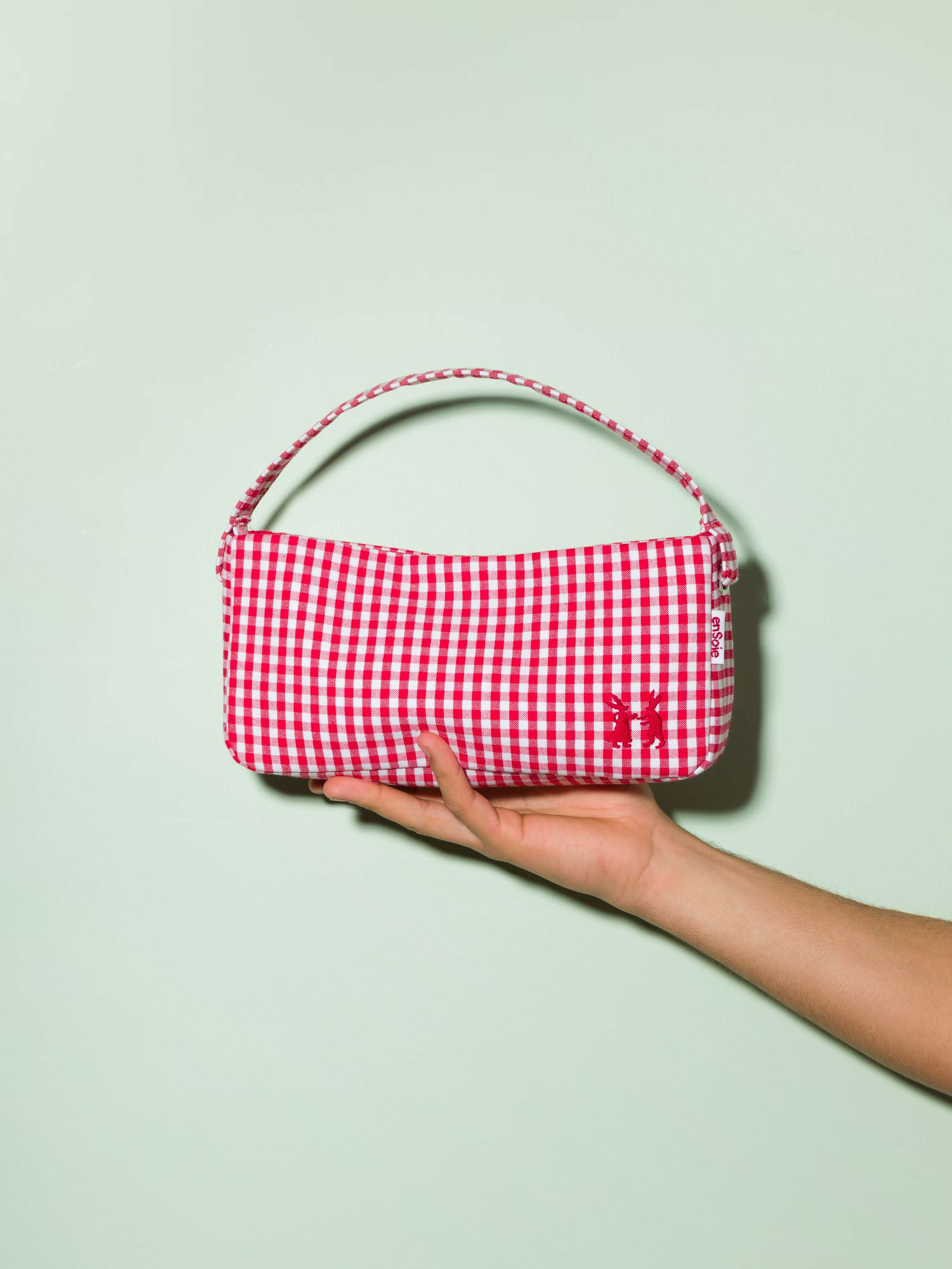 Picture of a hand holding a baguette bag made of cotton fabric featuring a red check pattern 